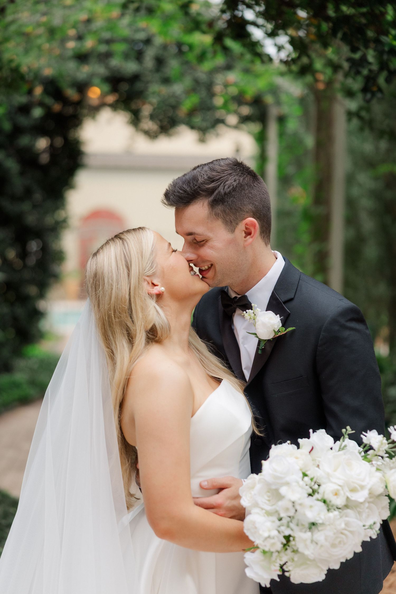 Wedding couple sharing romantic moments in a garden setting with white floral bouquet.