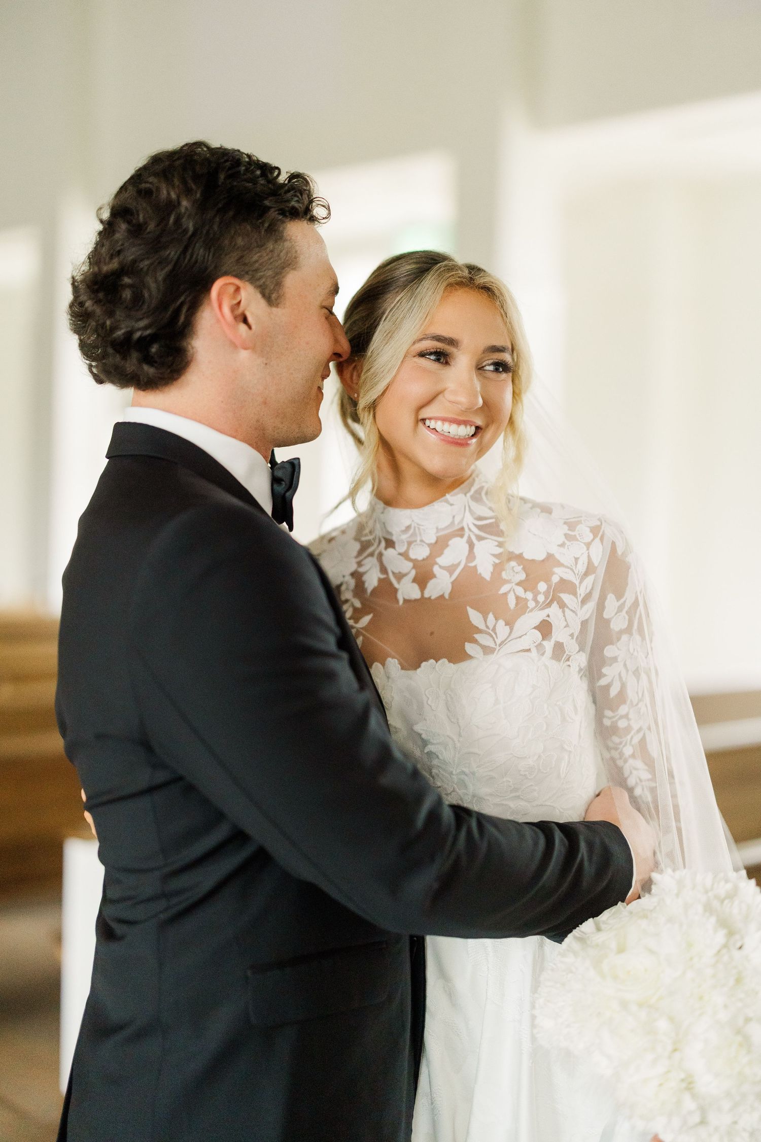 Joyful wedding couple sharing intimate moment in sunlit church corridor.