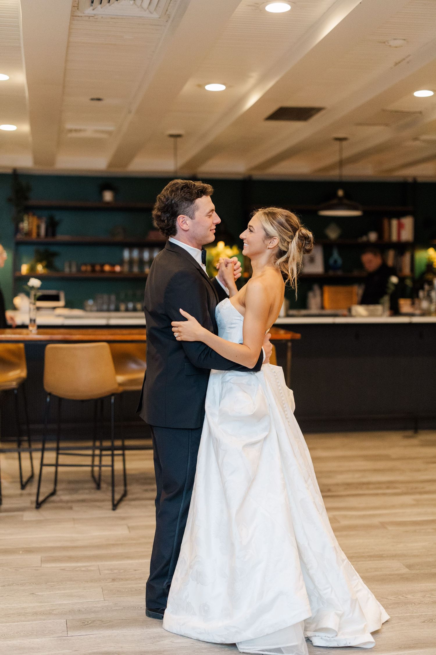 A couple shares their first dance in a modern reception venue with wood floors and ambient lighting.