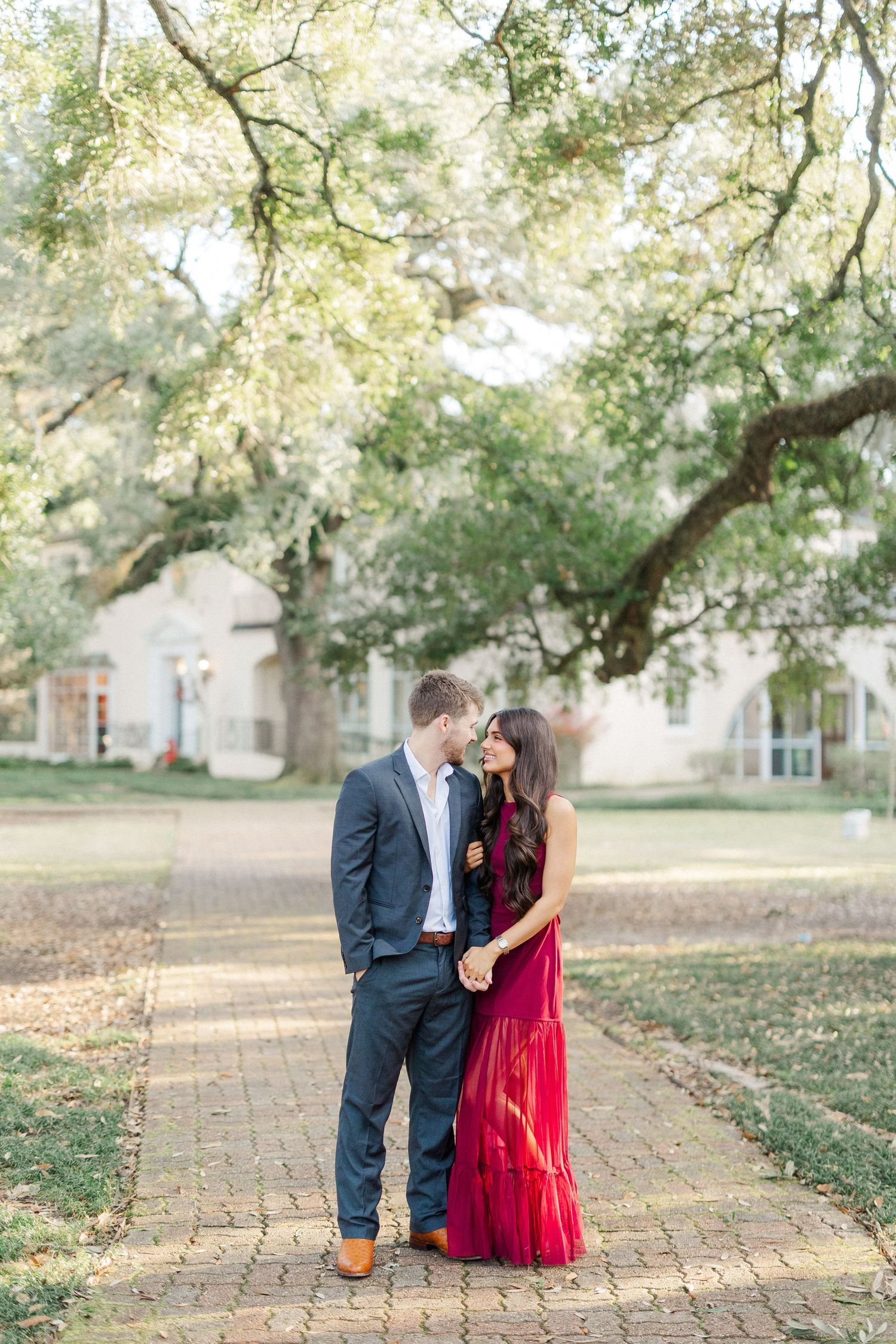 Couple in formal attire sharing a romantic moment on a brick pathway under trees at sunset.