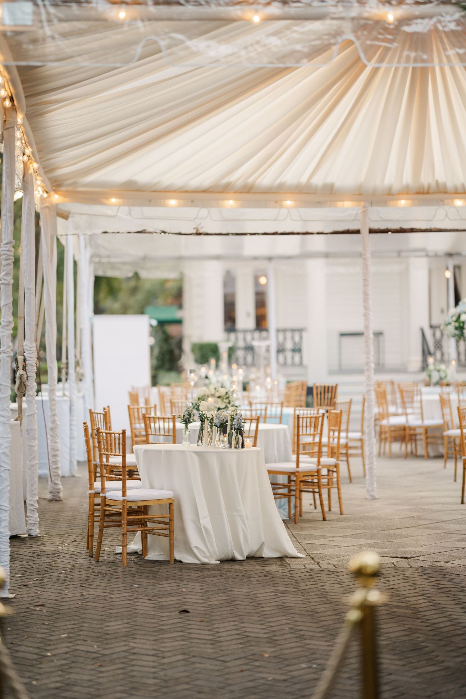 An elegant white wedding tent reception venue with draped fabric ceiling and wooden chairs.