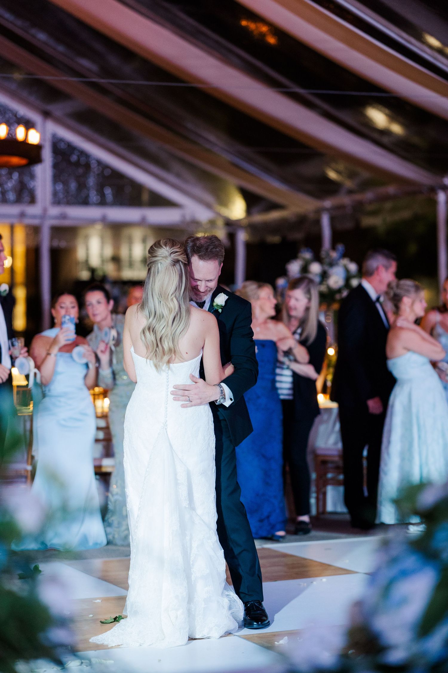 Wedding reception dance floor scene with couples dancing under twinkling lights and tent ceiling.