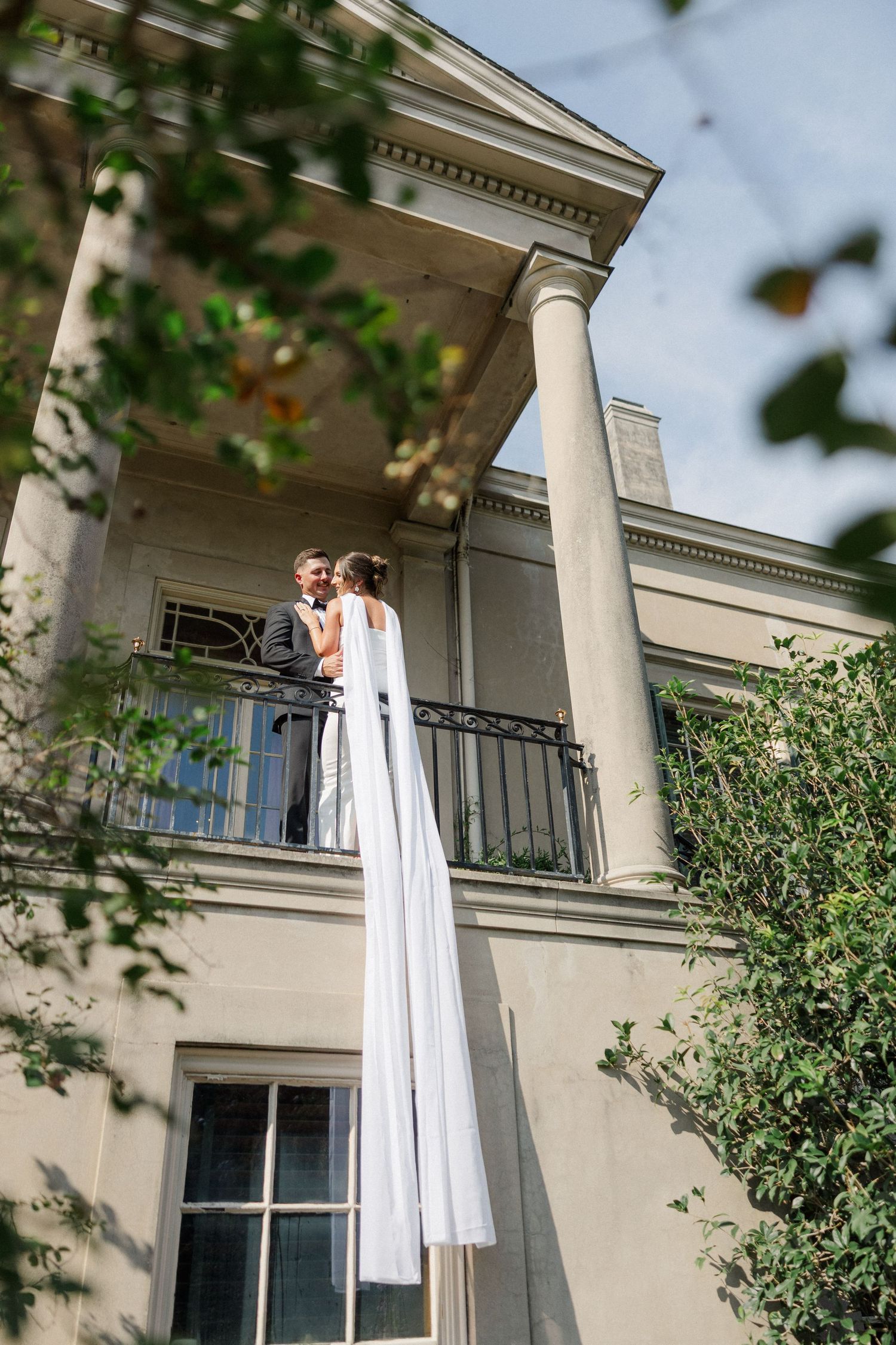 Elegant white mansion with classical columns and balconies draped with flowing white fabric in natural lighting.