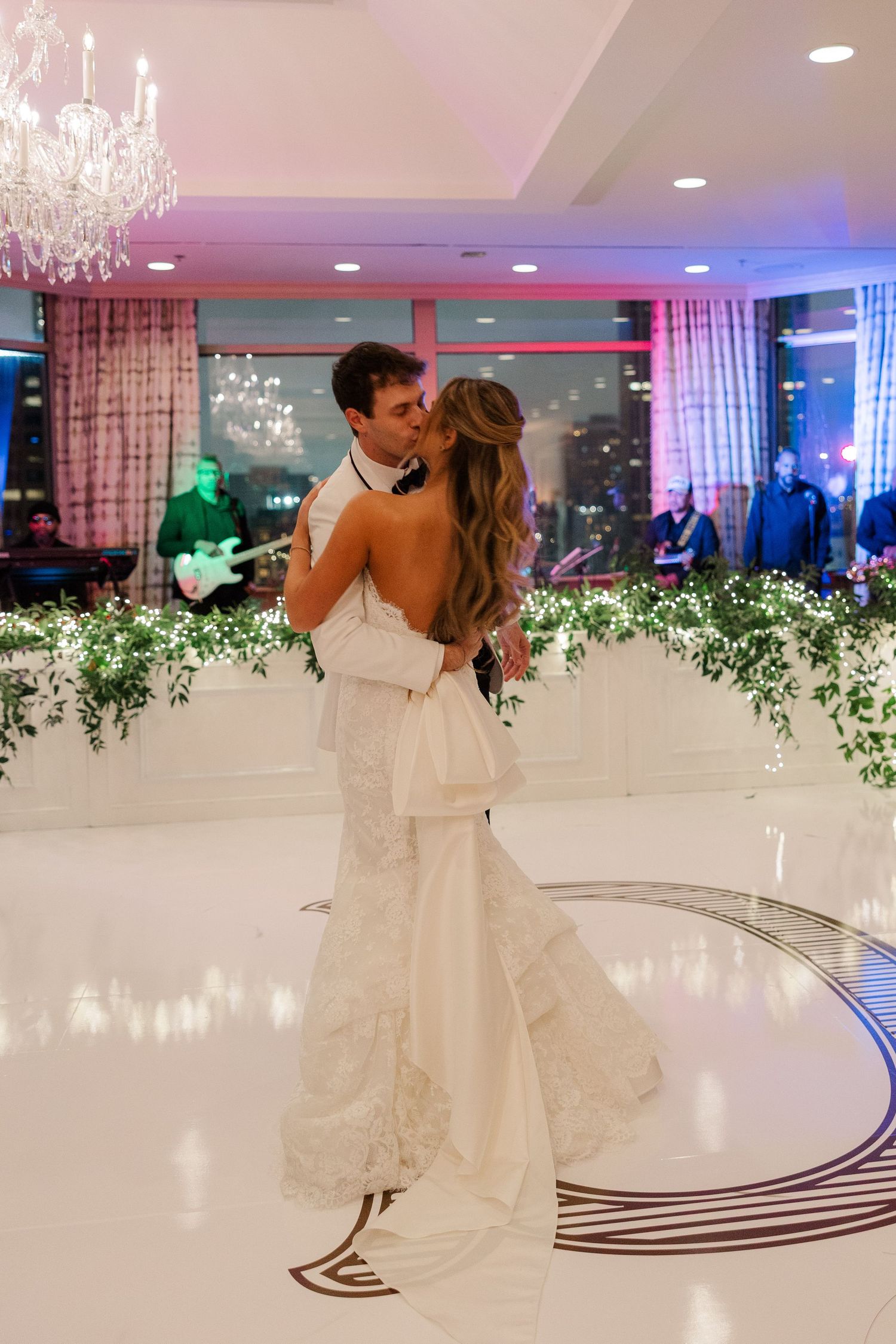Elegant wedding dance sequence on a white dance floor decorated with greenery and crystal chandeliers overhead.