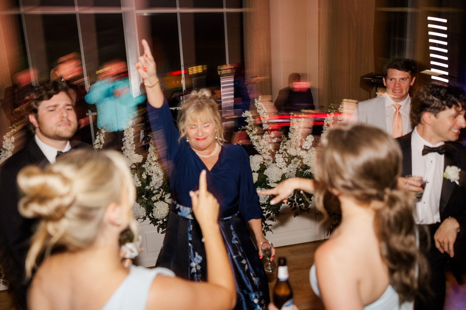 Elderly woman raises hand joyfully while dancing at festive wedding reception.