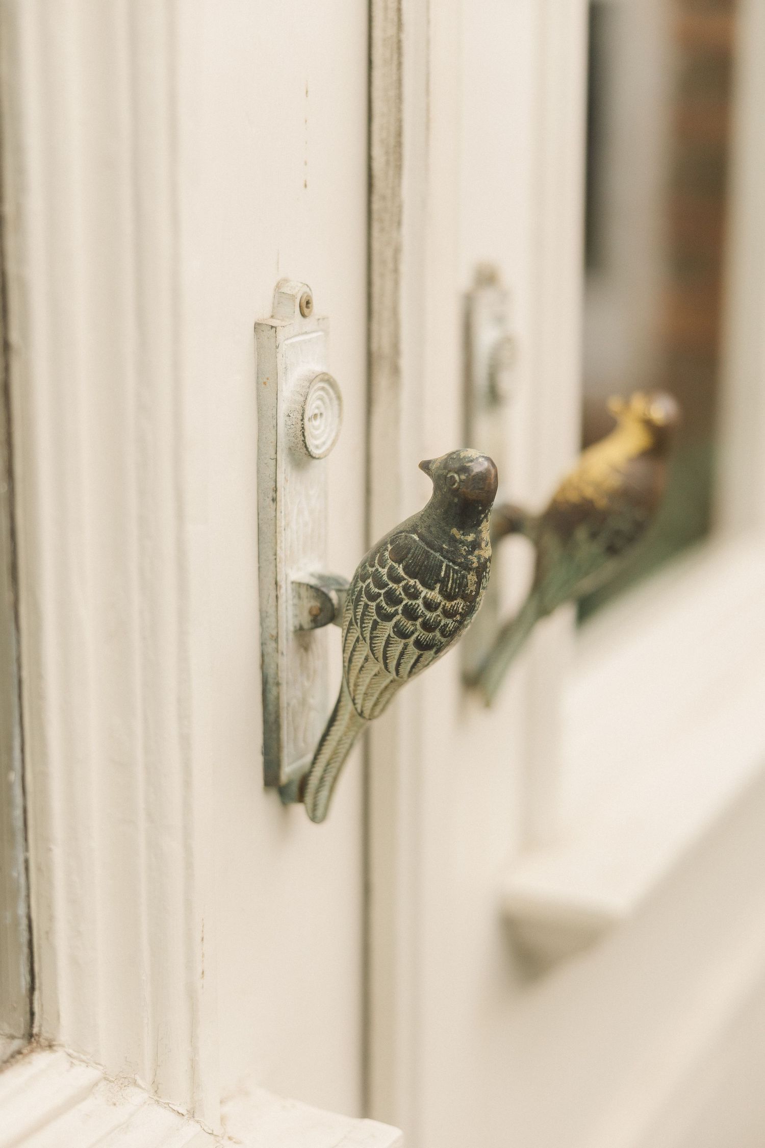 Vintage brass bird-shaped door knocker on a white painted wooden door with elegant detail.