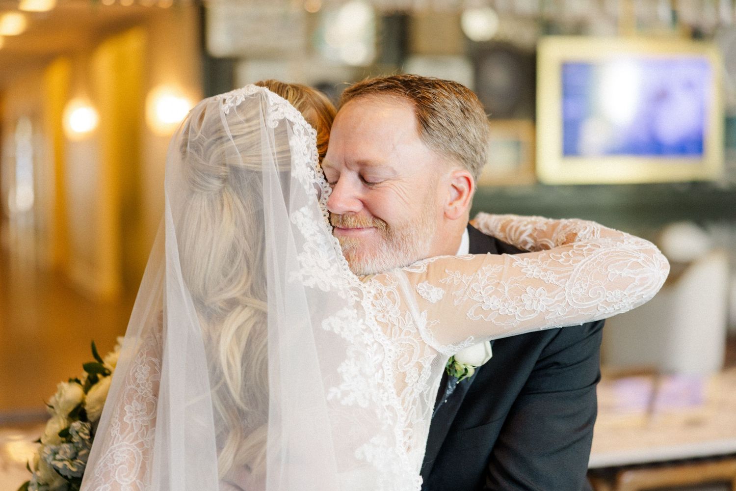 A romantic moment between a bride and groom as they share a tender embrace in a warmly lit indoor venue.