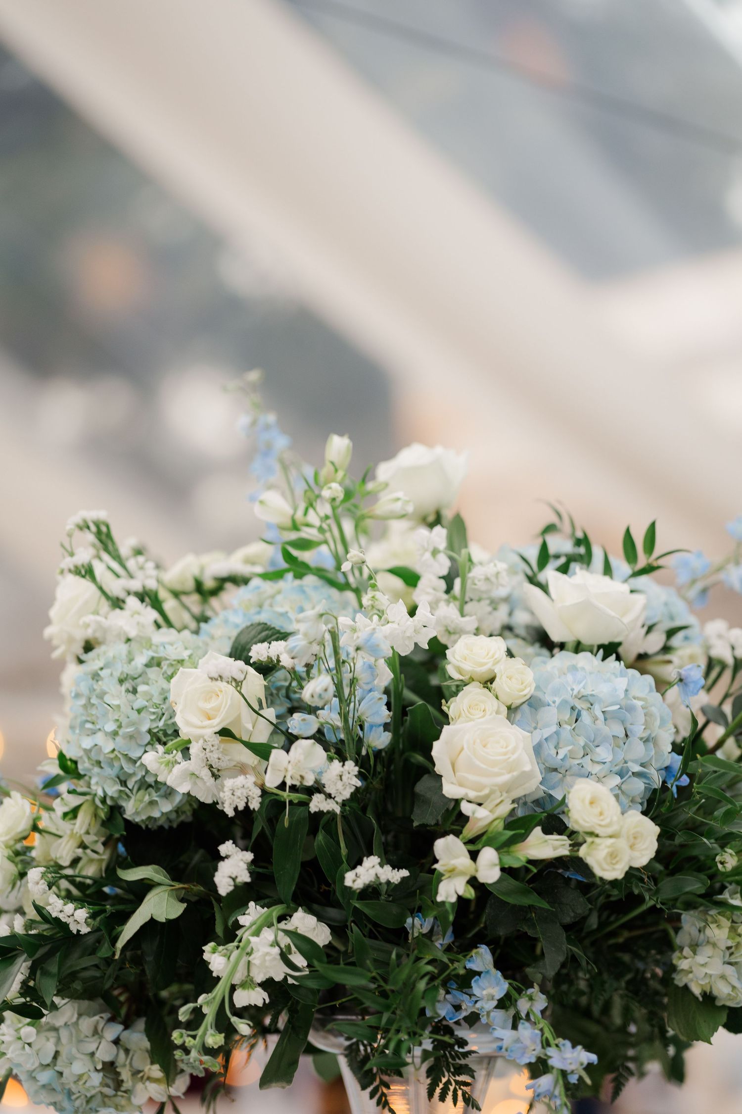 An elegant white and blue floral arrangement with roses, hydrangeas and delicate greenery.