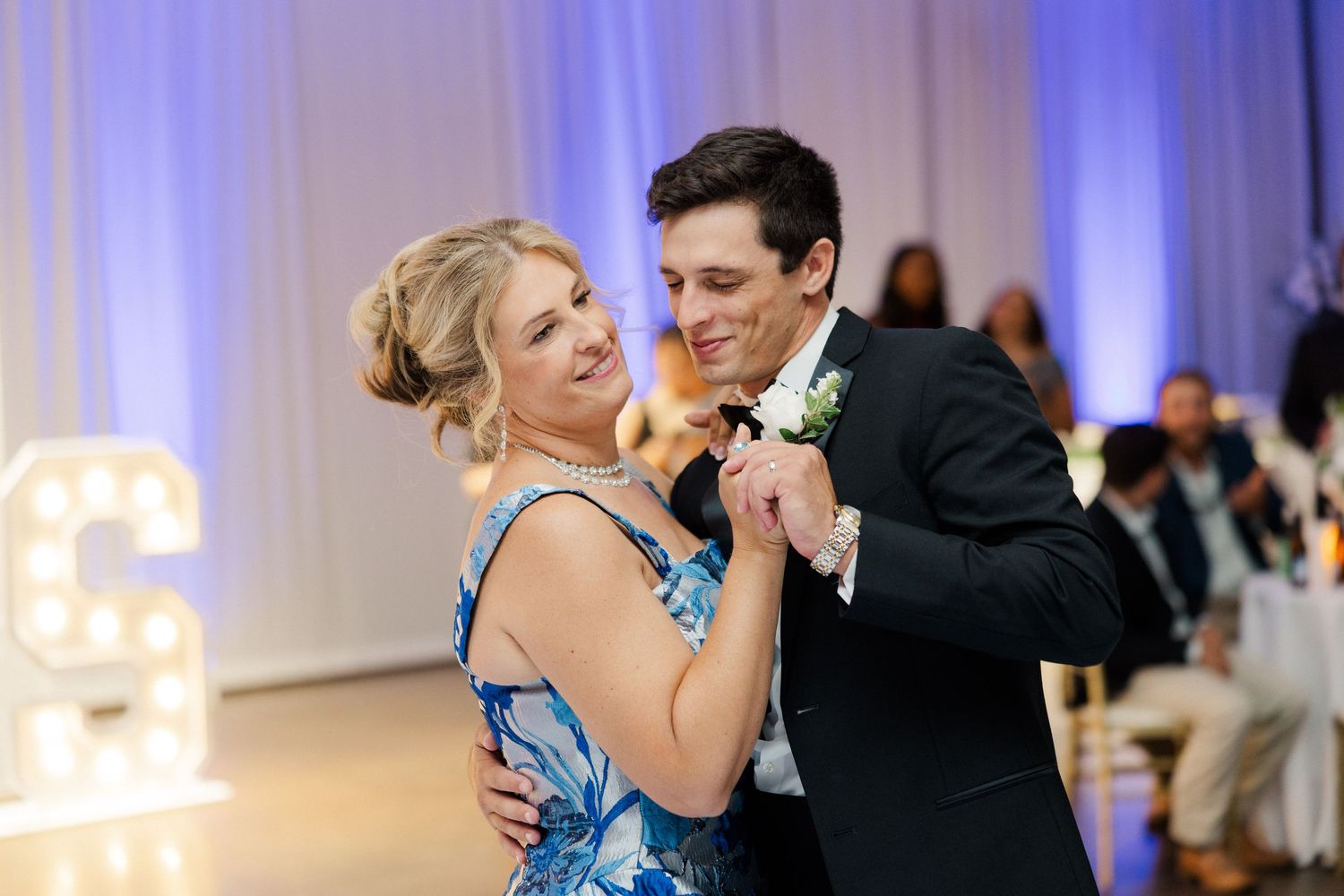Couples slow dancing at an elegant wedding reception with blue ambient lighting.