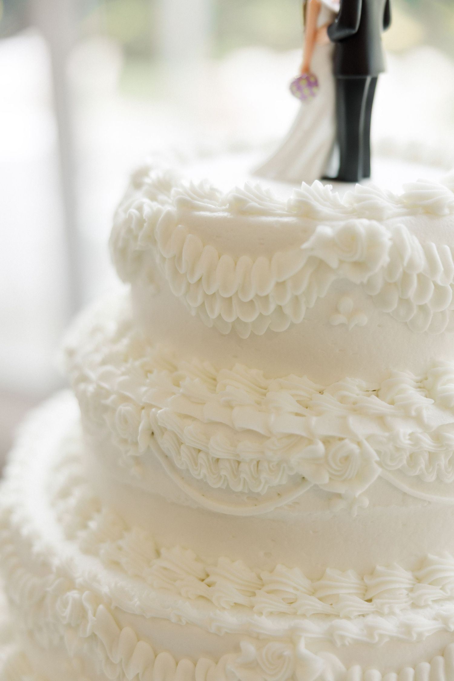 Close-up details of a white wedding cake with delicate ruffled frosting tiers and elegant piping work.