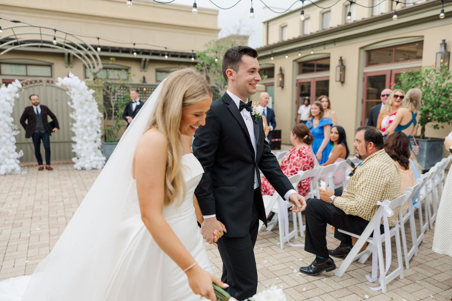 Wedding ceremony setup with white chairs and floral decorations in an elegant outdoor space.