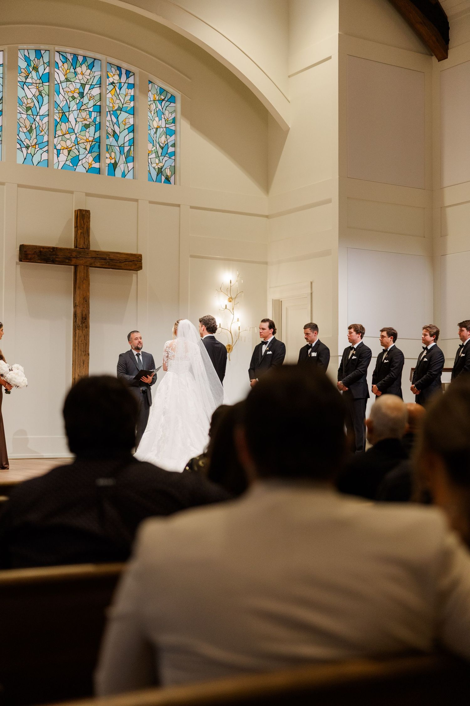 A traditional church wedding ceremony with guests seated and a wooden cross on the altar wall.