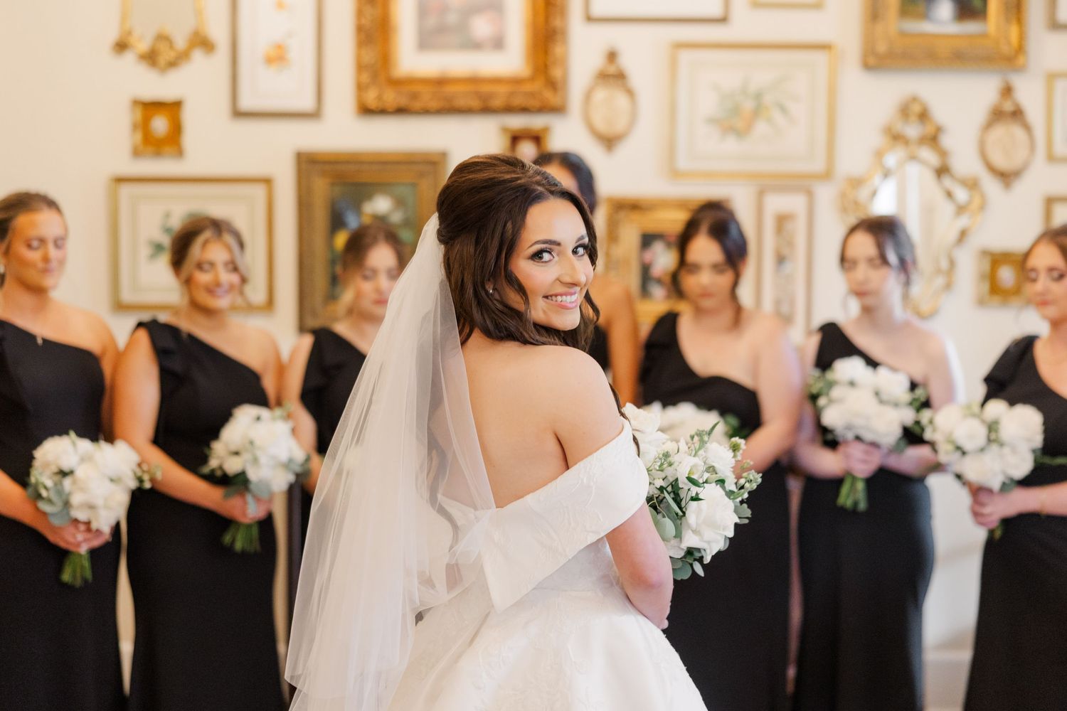 Elegant wedding party poses in an ornate room with gold-framed artwork and classical decor.