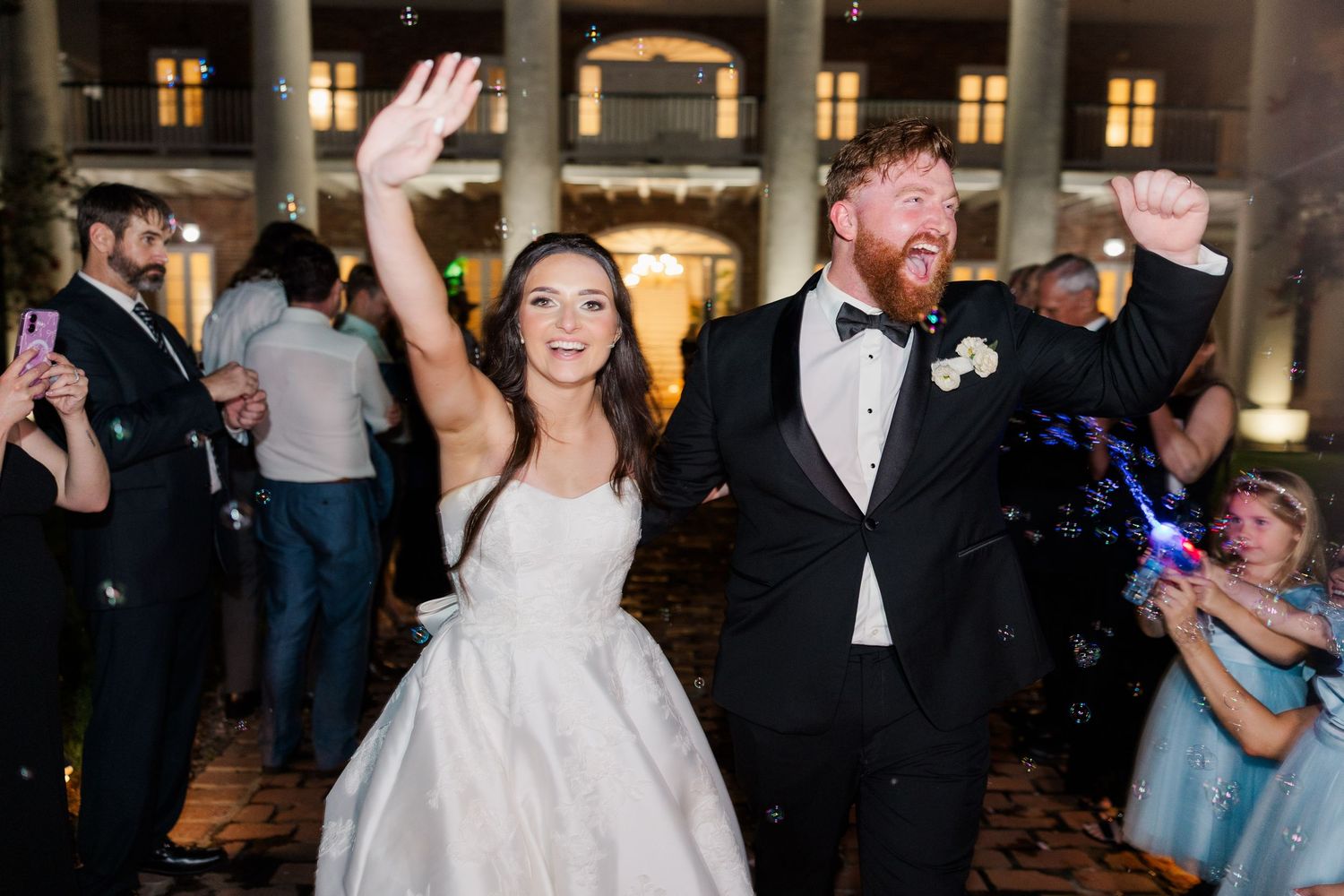 Wedding celebration in an ornate venue with columns and warm lighting as guests dance and celebrate.