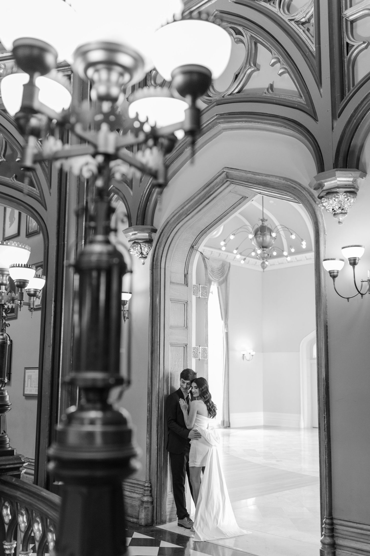 Black and white wedding photo captured on an ornate grand staircase with vintage light fixtures and elegant architectural details.