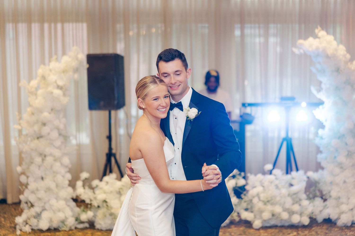 Newlyweds dance together at their reception with white floral arrangements in the background.