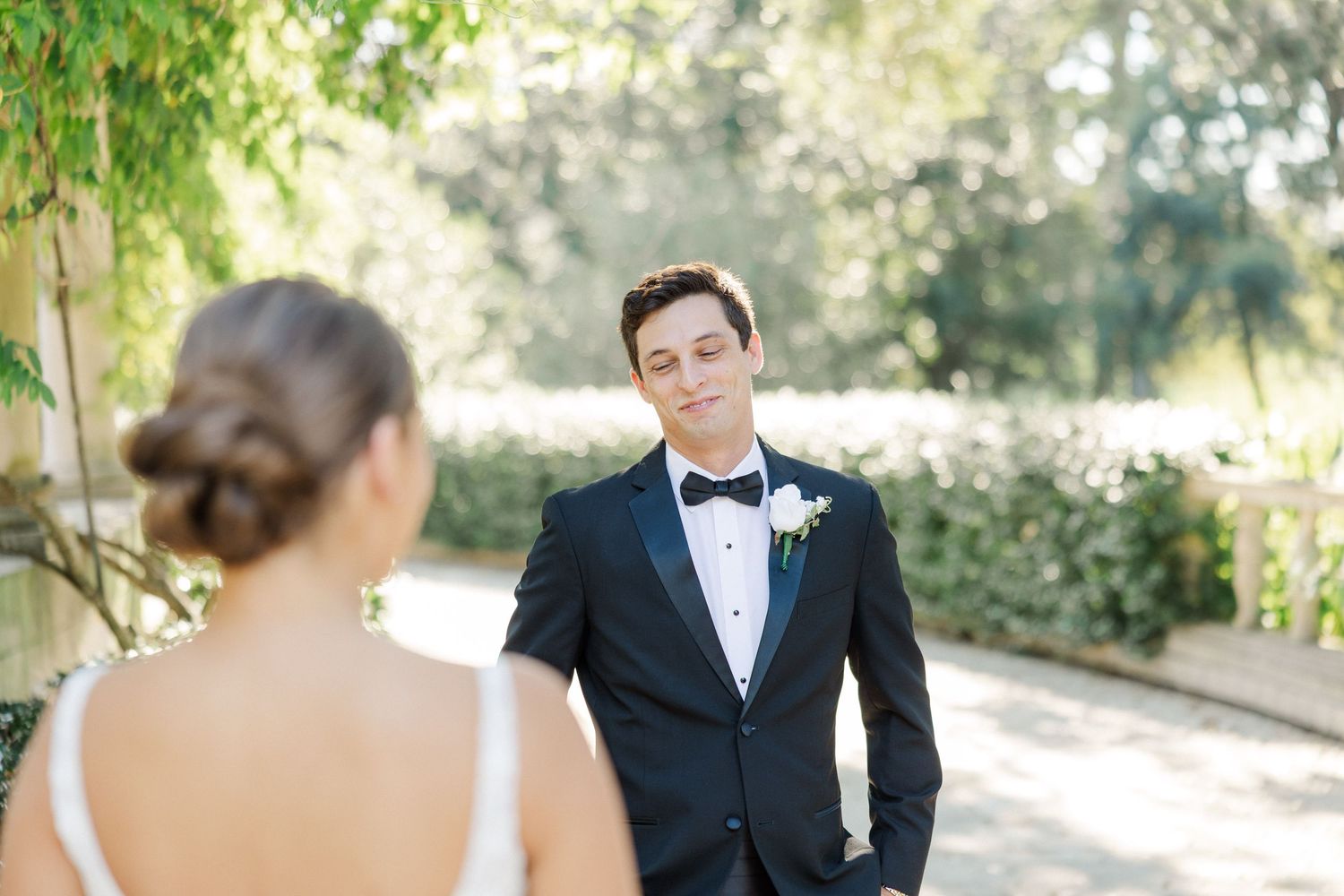 An outdoor wedding ceremony setup with guests seated in white chairs among lush greenery.