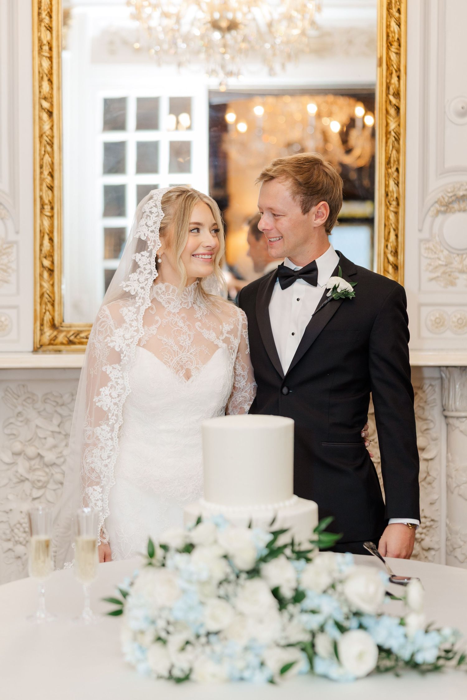 Romantic wedding moment by an elegant white cake with blue and white floral decorations.