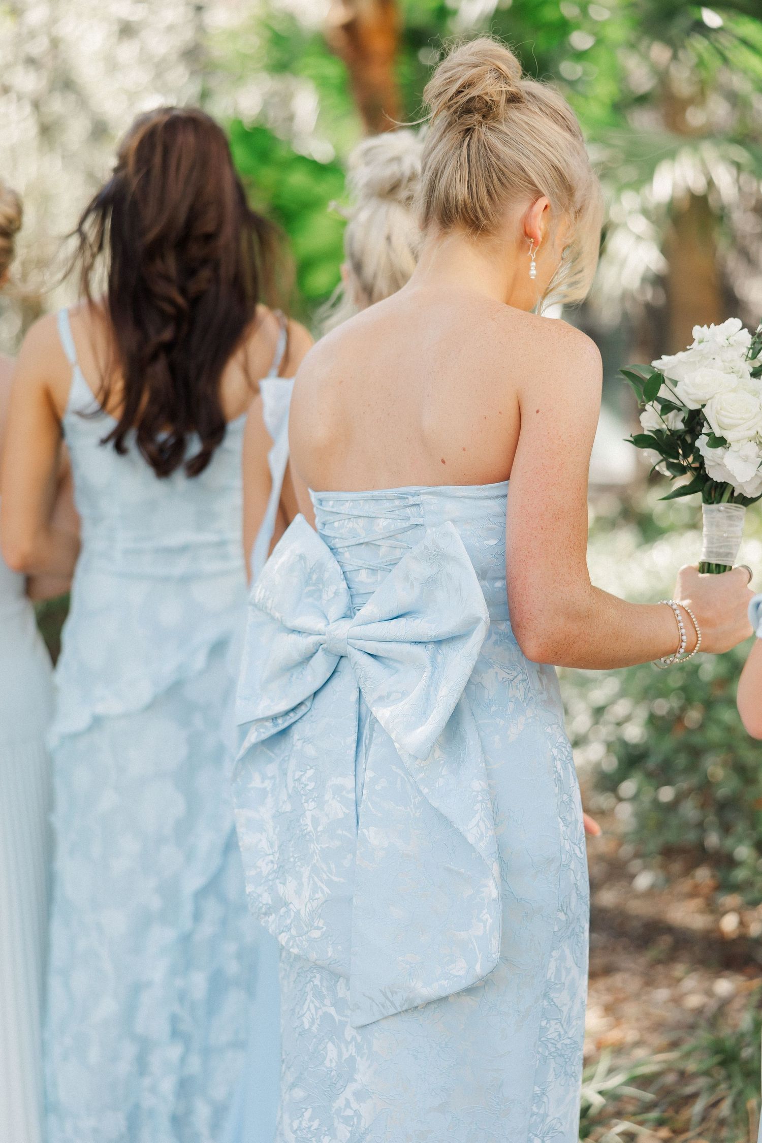 Light blue bridesmaid dresses with elegant bow details and floral patterns shown from behind.