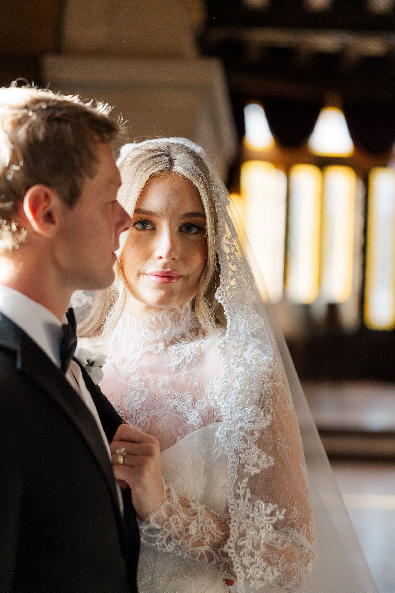 Intimate wedding portrait showing elegant lace veil details in warm indoor lighting.