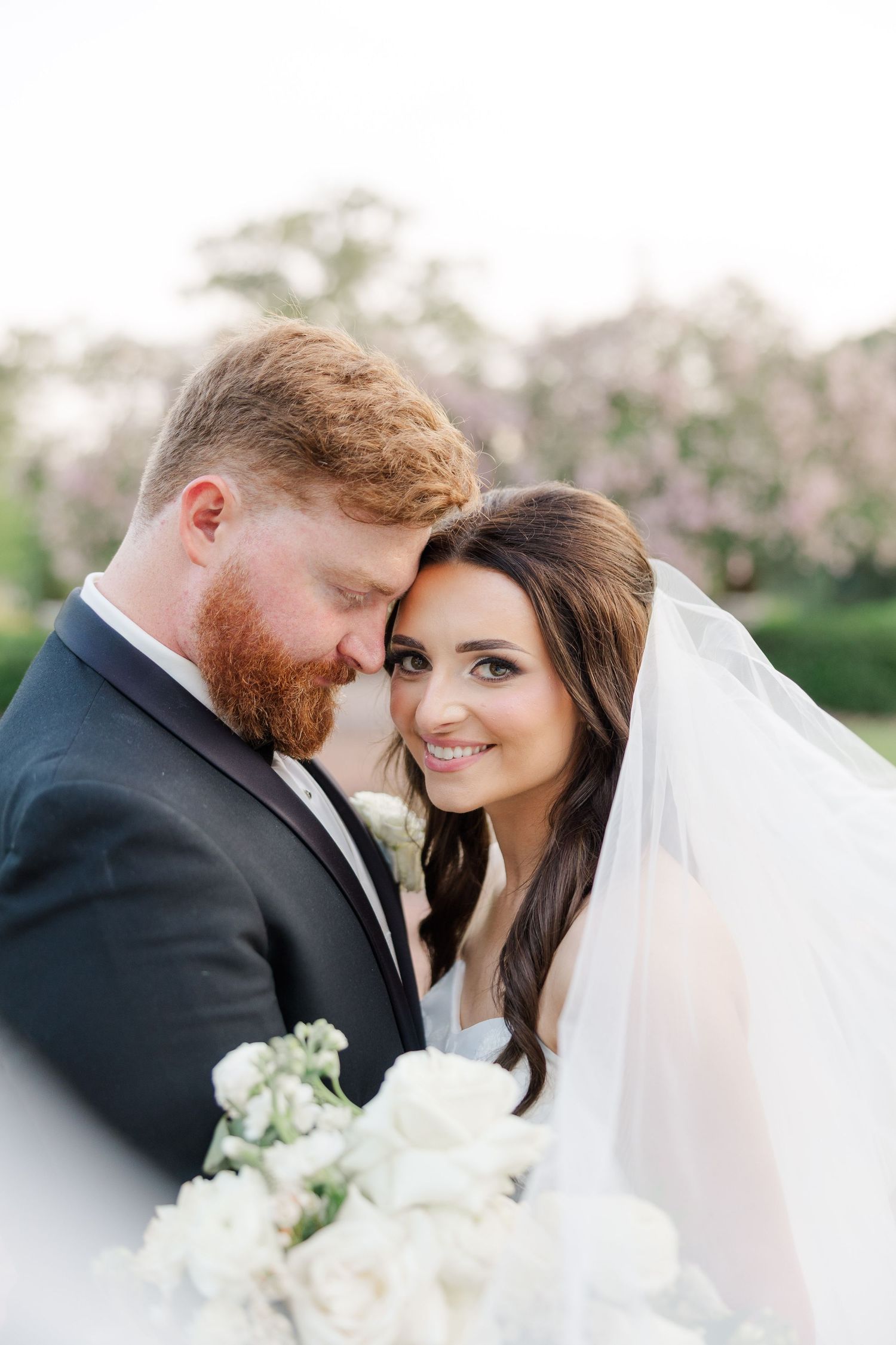 Intimate wedding portrait of newlyweds embracing outdoors with white floral bouquet.