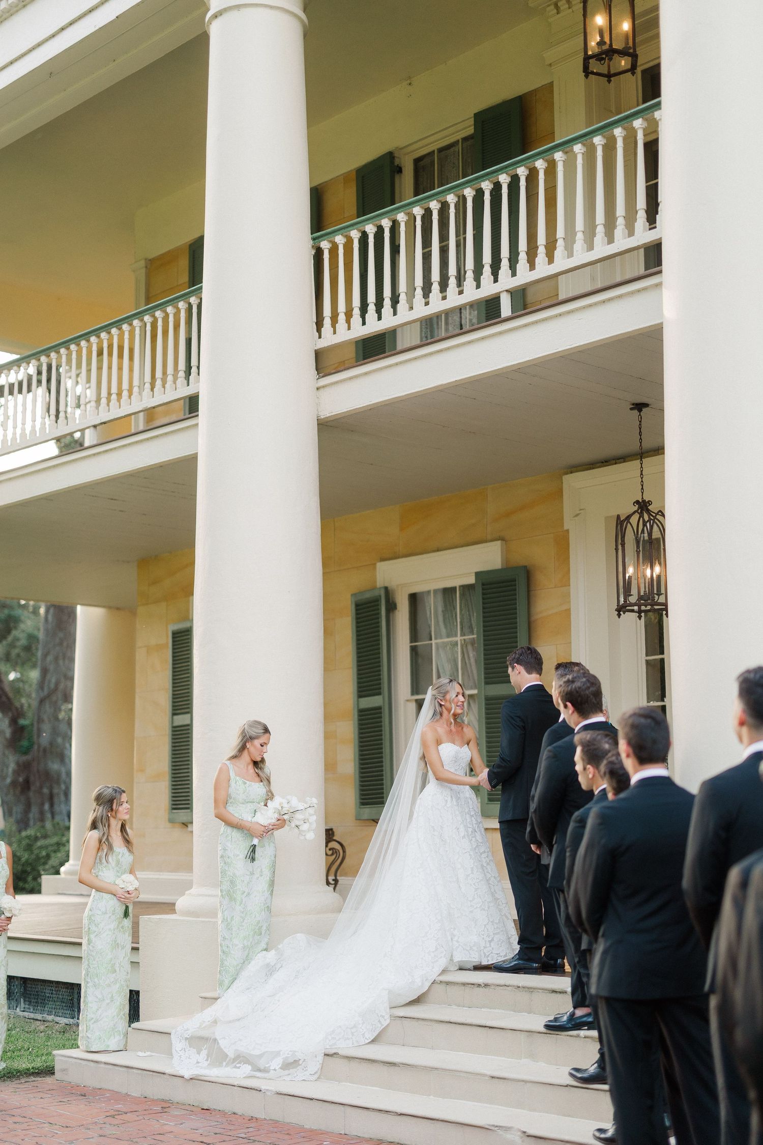 Bride and groom exchange vows on steps of grand white-columned Southern plantation estate.
