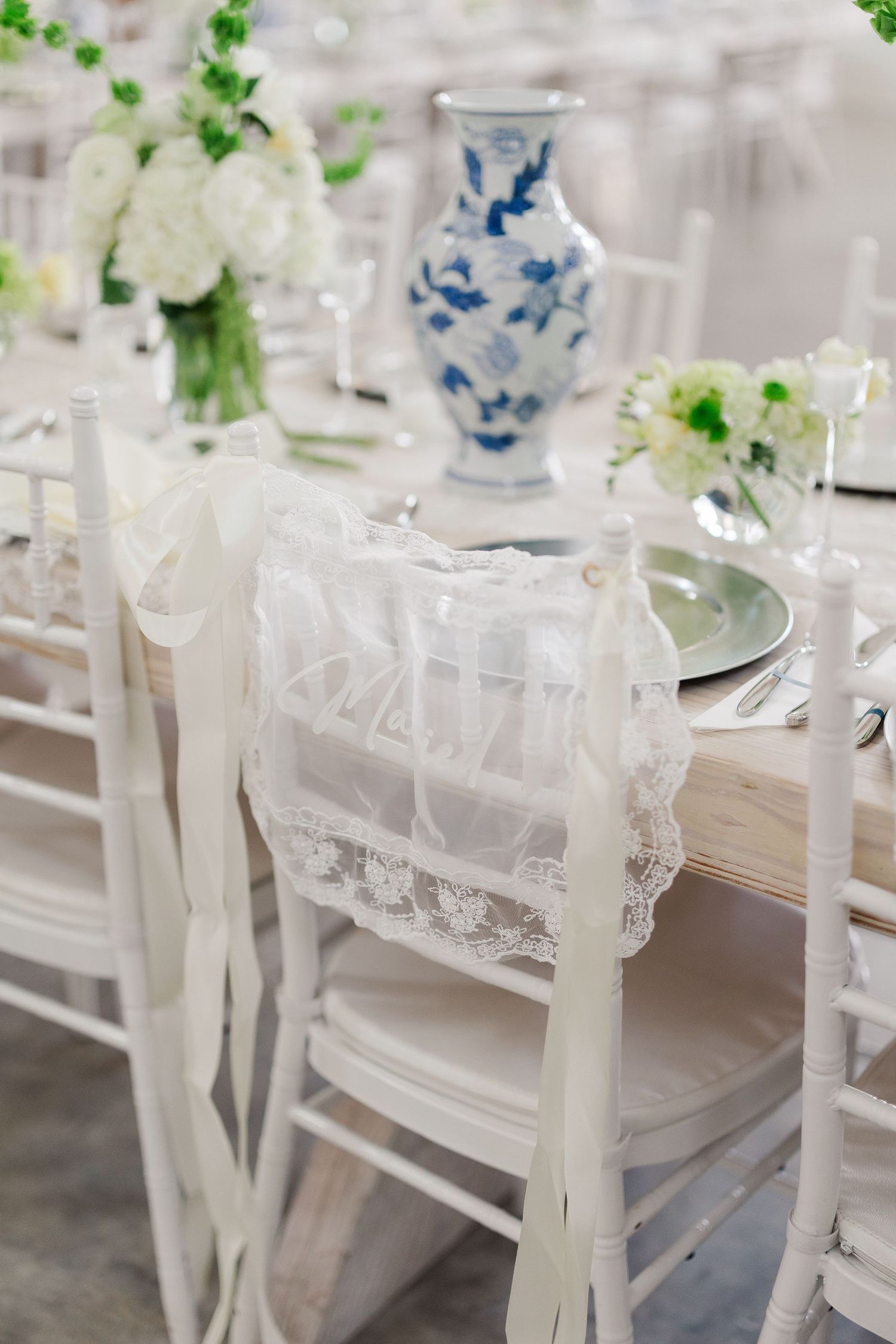White chiavari chair with lace ribbon detail at elegant wedding reception with blue and white vase centerpiece.
