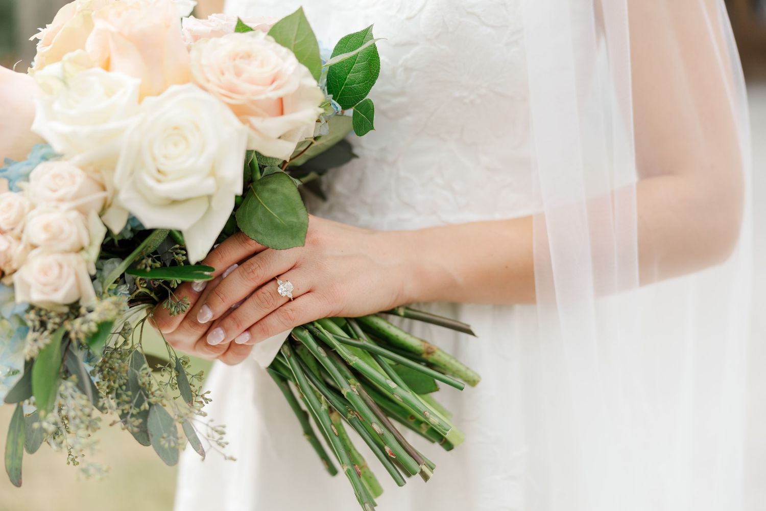 Beautiful bridal bouquet of soft pink and white roses with eucalyptus greenery held against white wedding dress.