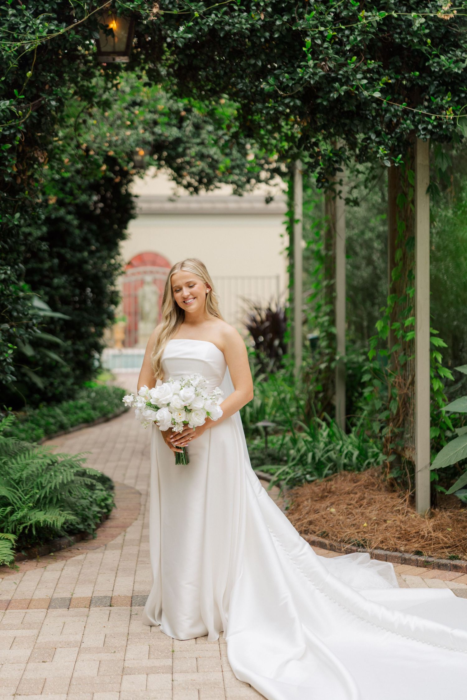 Wedding dress with flowing train photographed in a garden setting with lush greenery.