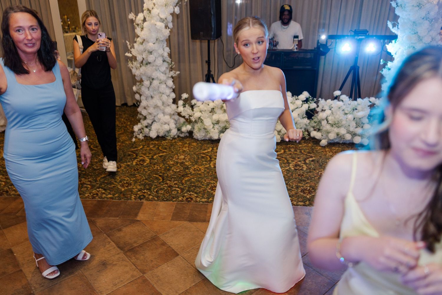 Reception celebration with guests dancing and white floral decorations in an elegant ballroom.