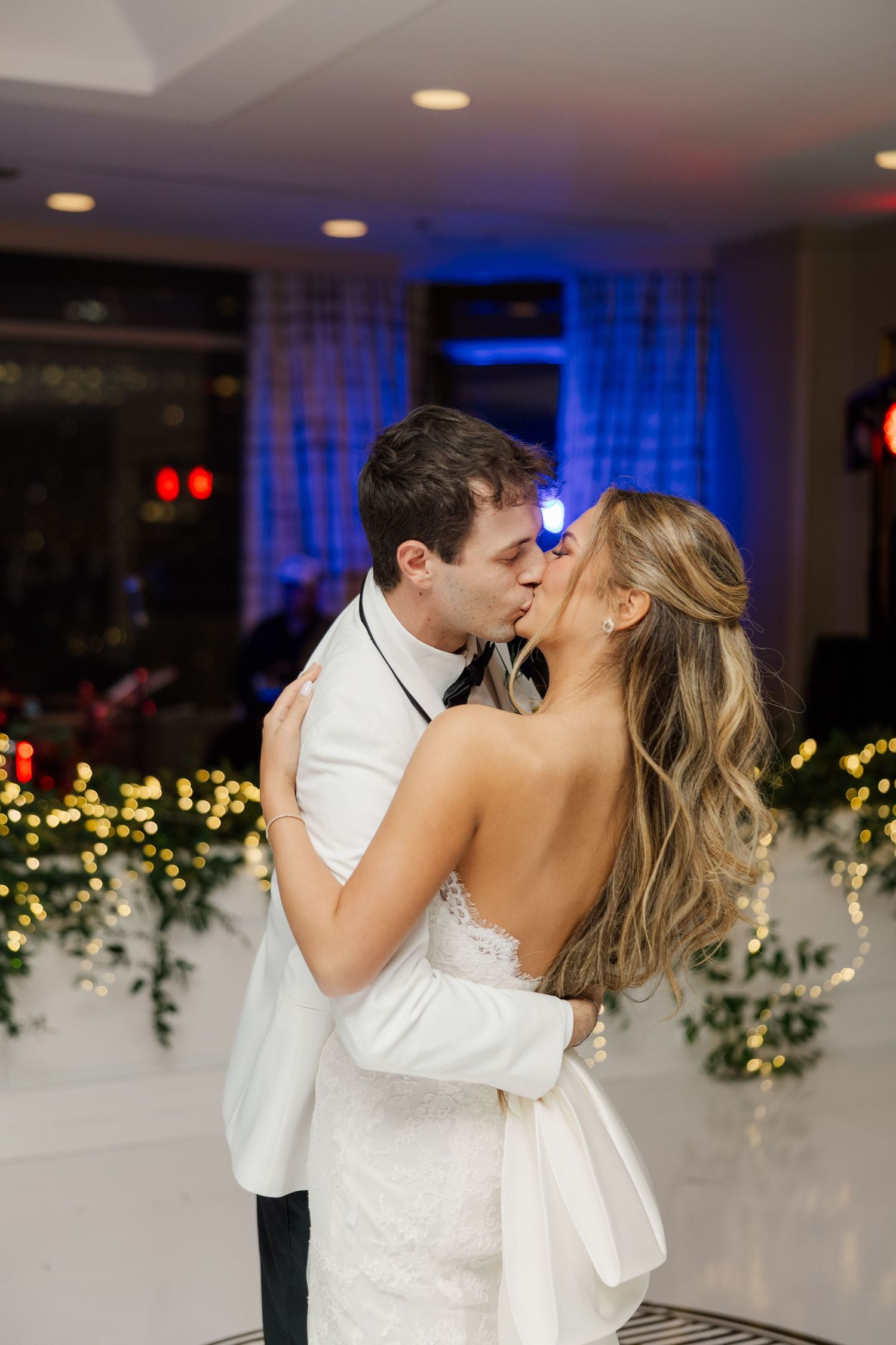 Romantic first dance between newlyweds with twinkling lights in the background.