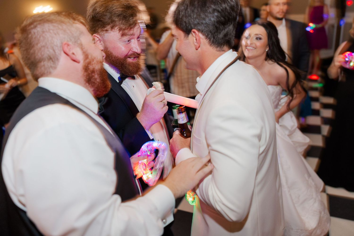 Wedding reception guests dancing and celebrating on checkered dance floor with party lights.
