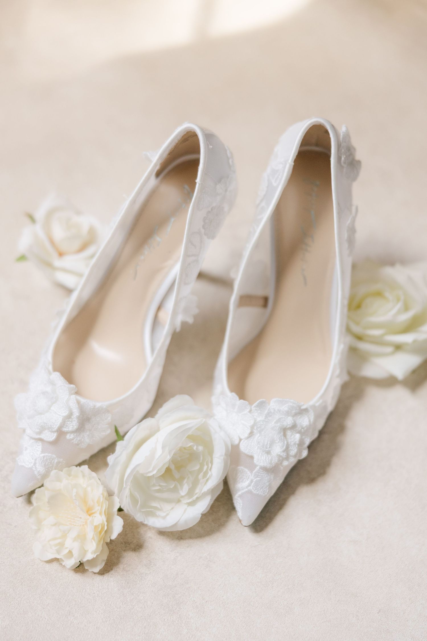 Elegant white bridal shoes with delicate lace details and floral embellishments displayed in a row.