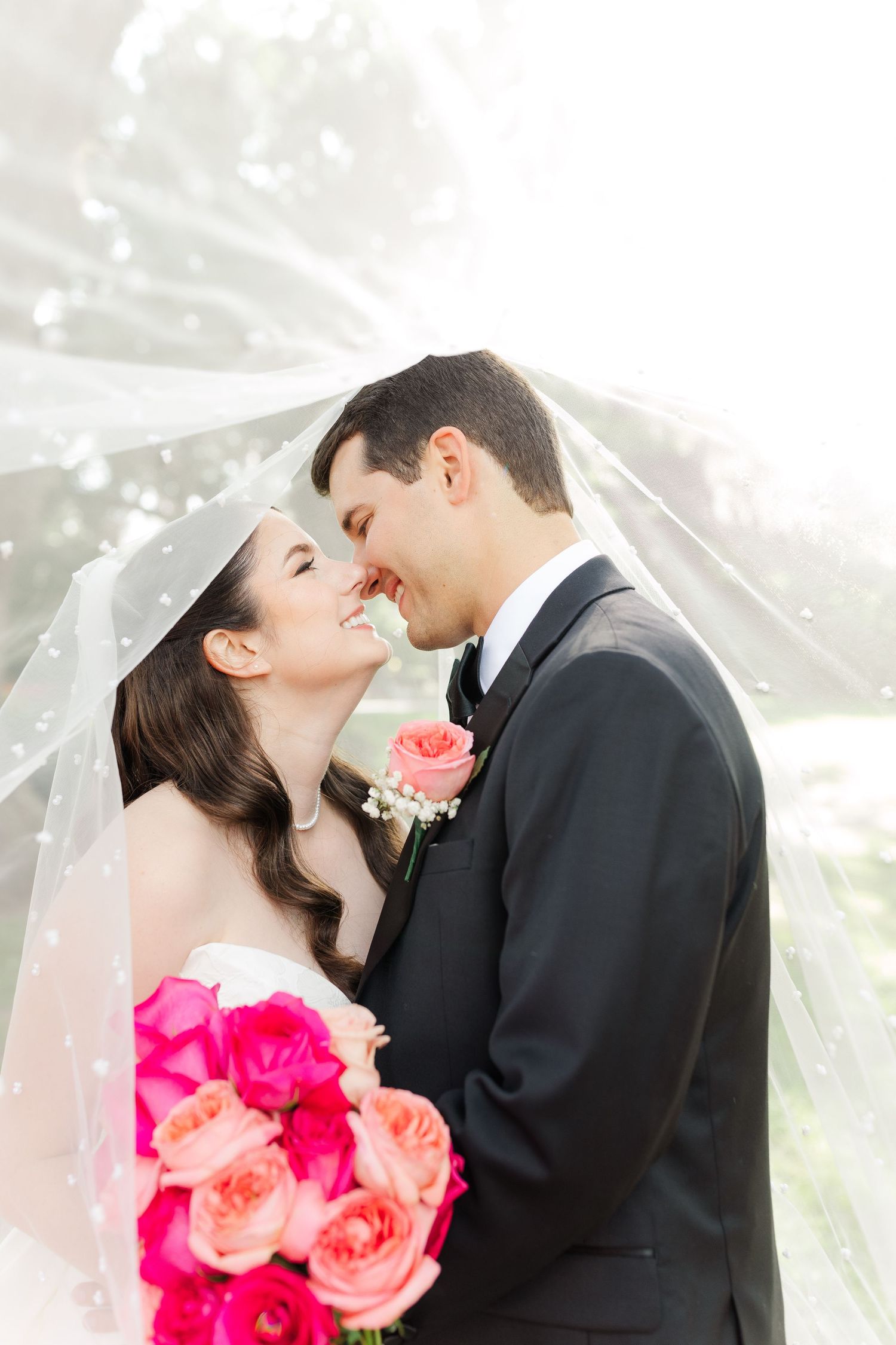 Wedding couple with bright pink bouquet sharing intimate moment under flowing veil.