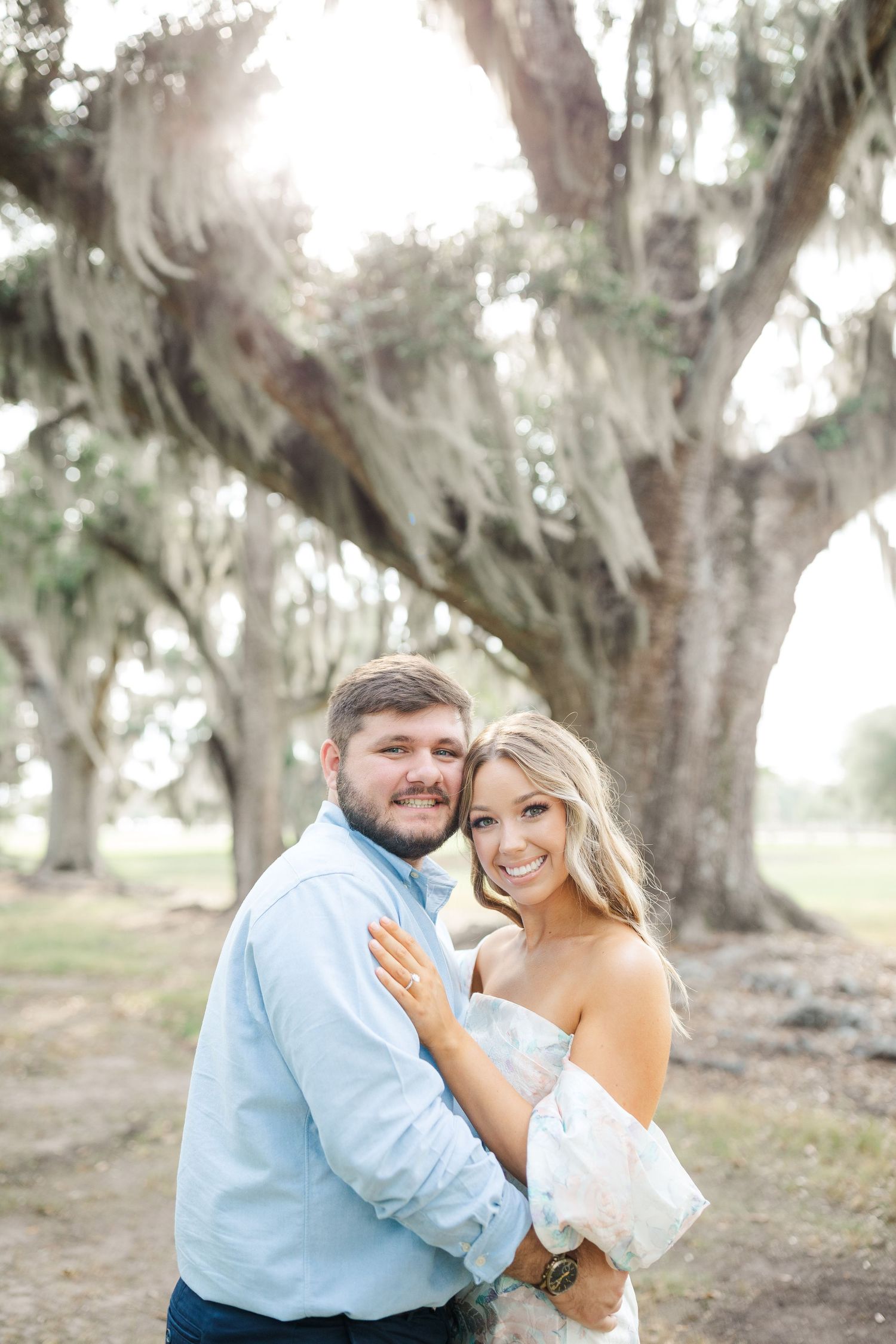 A couple poses together under a majestic Spanish moss-draped oak tree in a romantic outdoor setting.