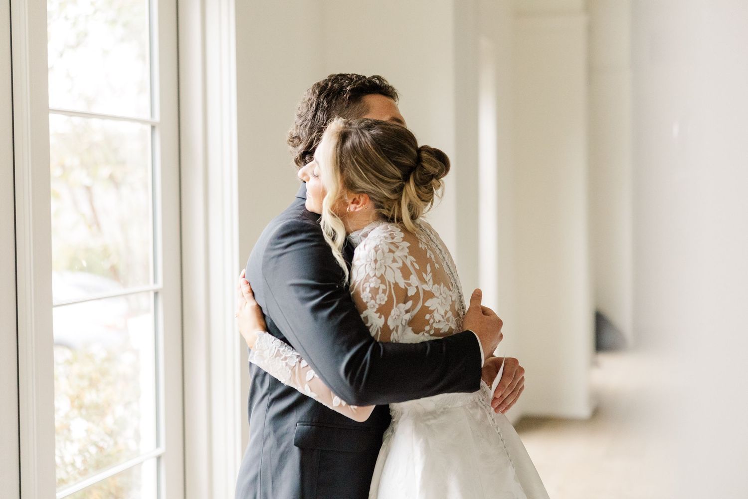 A romantic first look between newlyweds in a sunlit white hallway.