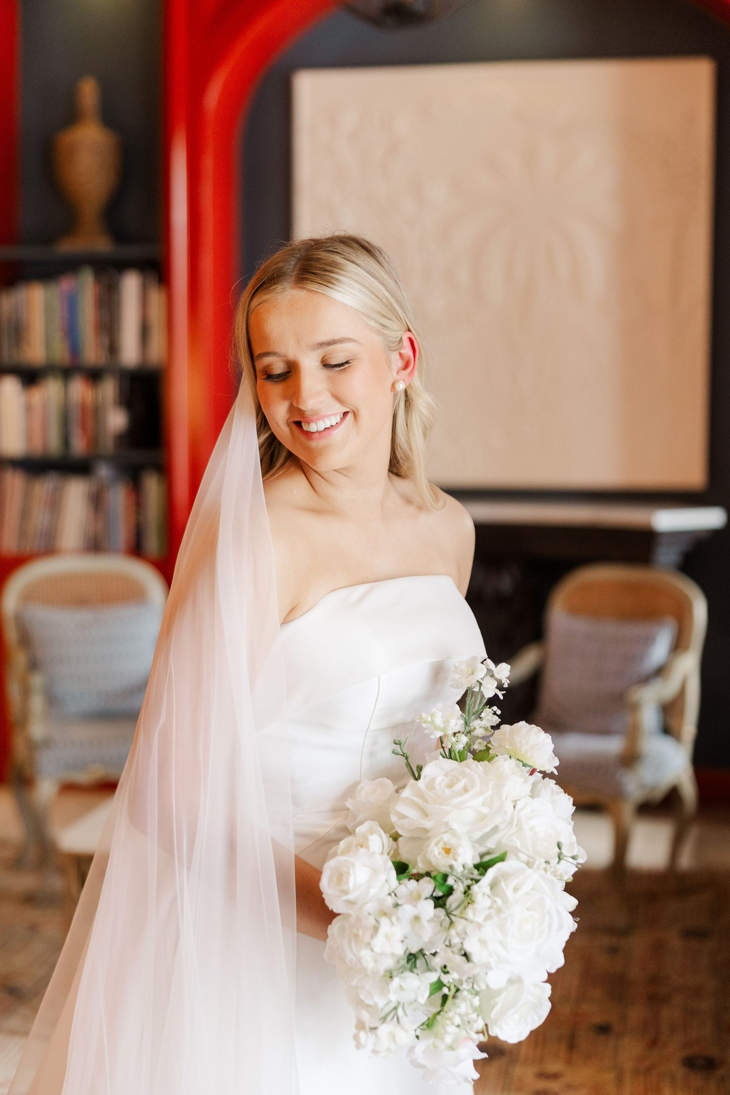 A bride in a white wedding dress holds a beautiful bouquet of white flowers while posing indoors.