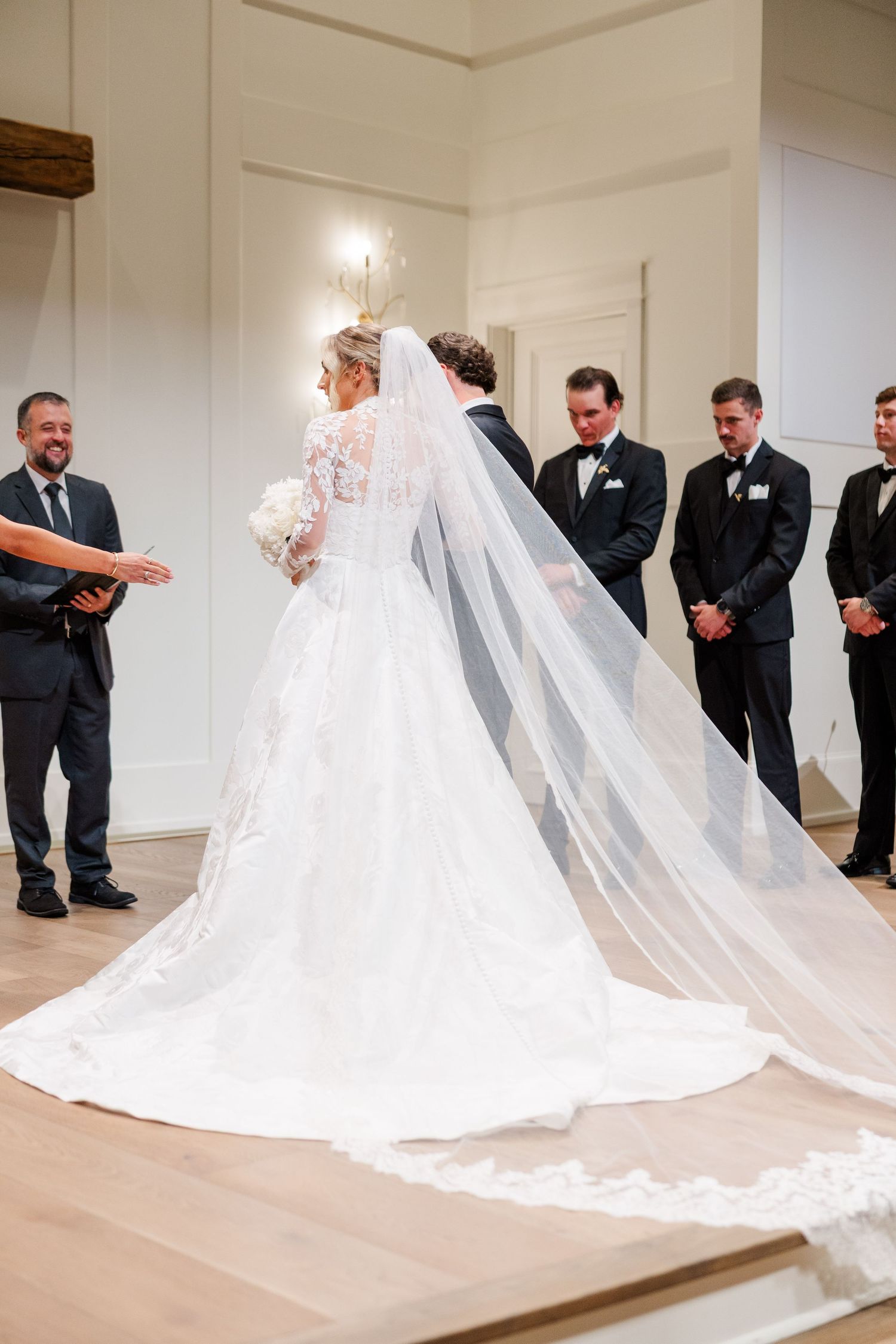 A flowing cathedral veil trails behind a white wedding dress during a ceremony.