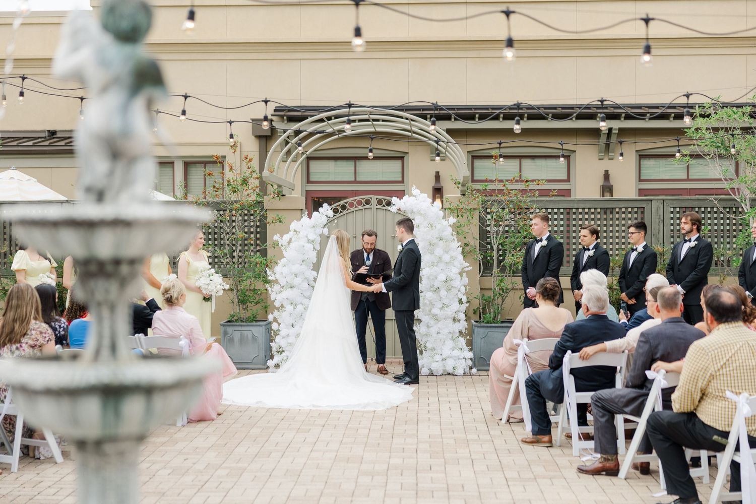 Outdoor wedding ceremony setup with white chairs and stone architecture in the background.