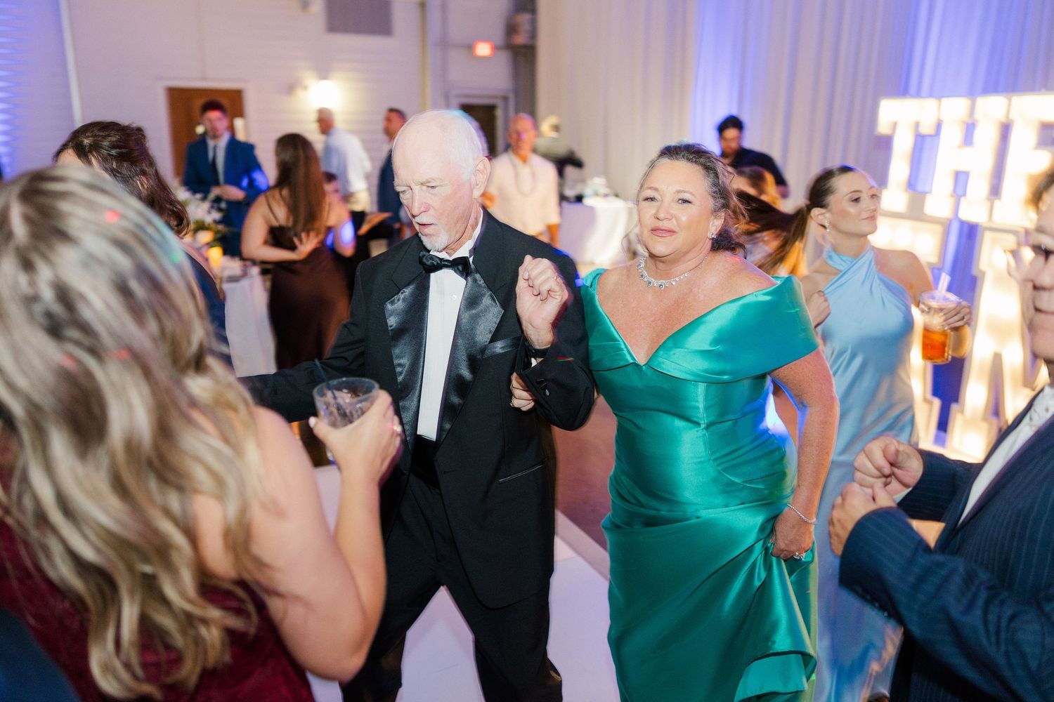 Wedding reception guests dancing and celebrating on a lively dance floor with blue lighting.