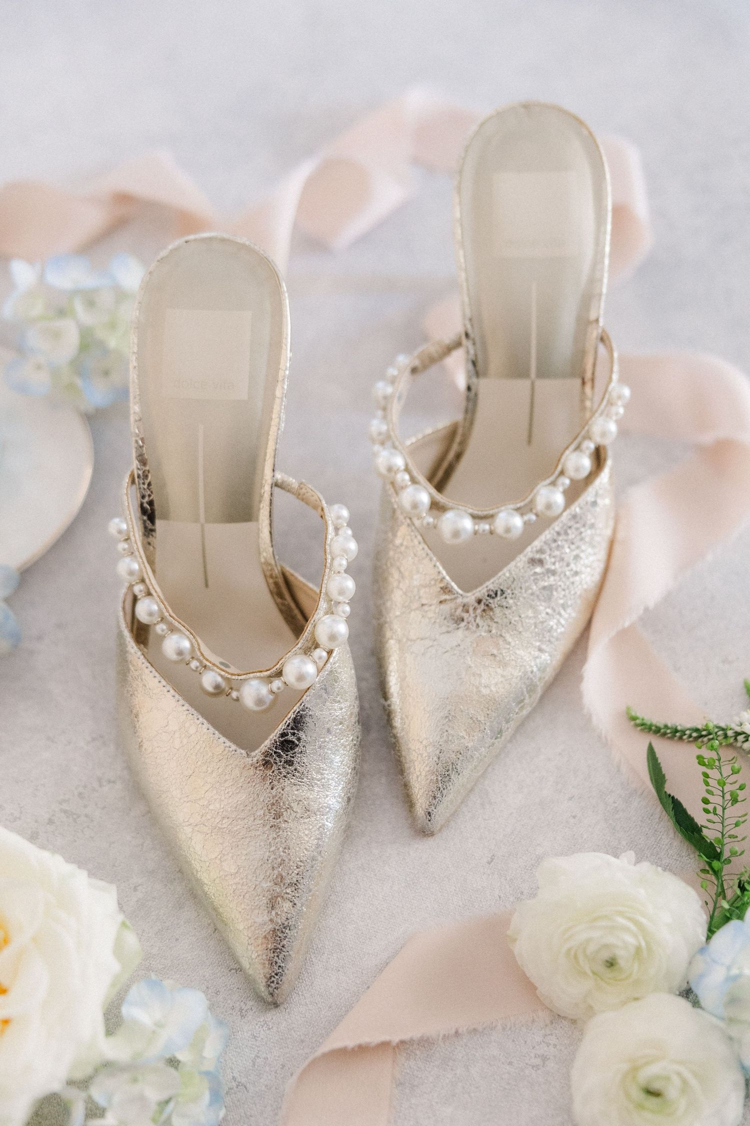Elegant silver glitter wedding shoes with pearl details displayed with white roses on blush pink fabric.