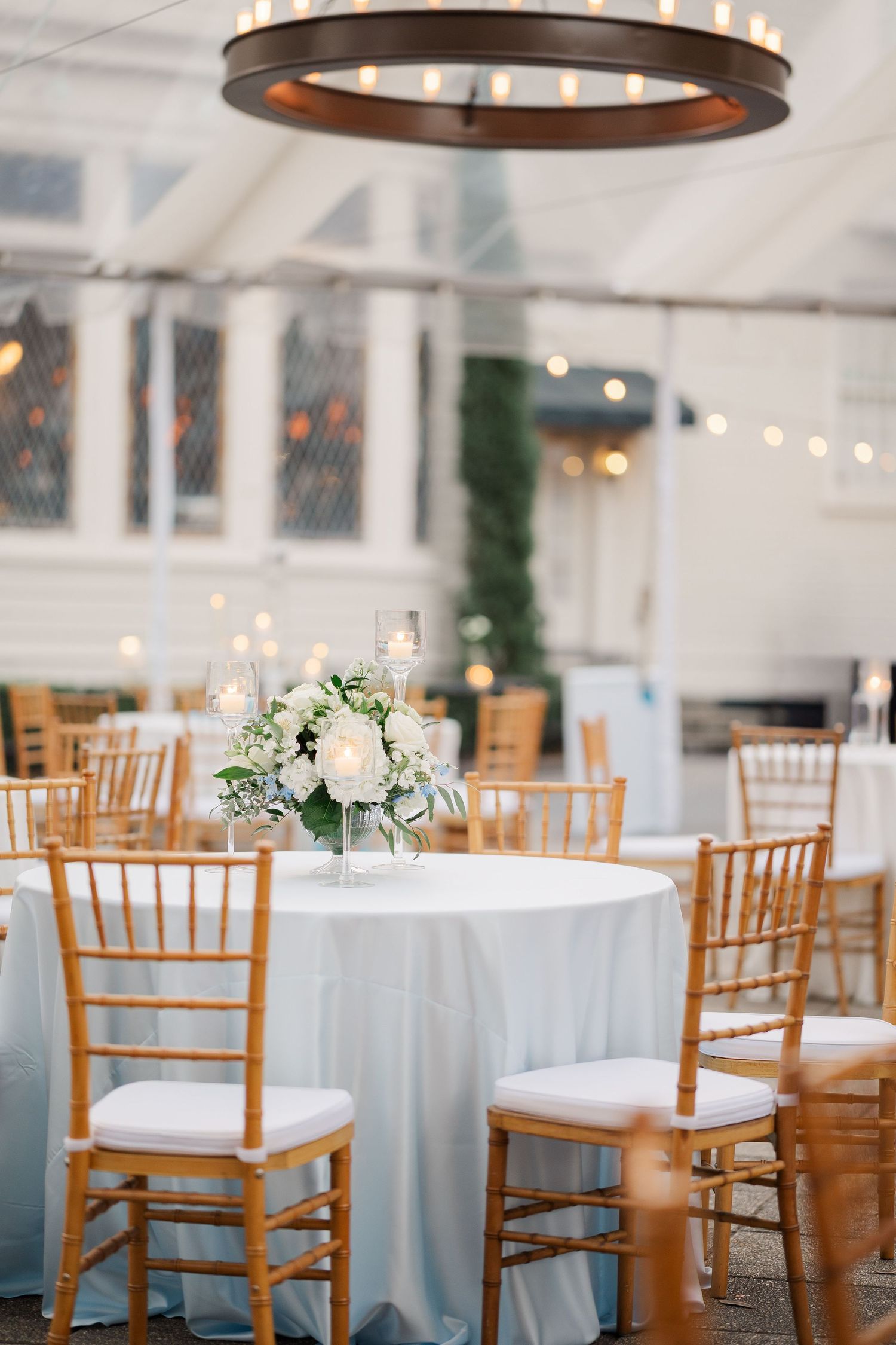 Wedding reception venue with light blue tablecloths and wooden chiavari chairs.