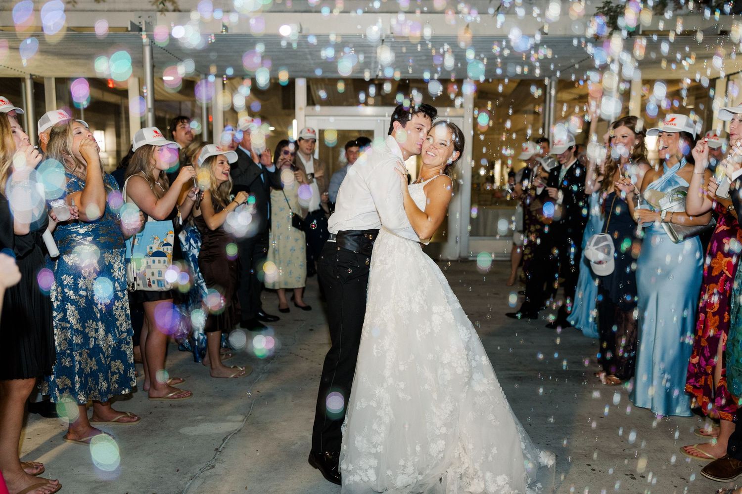 Wedding exit celebration with bubble send-off and guests in formal attire.