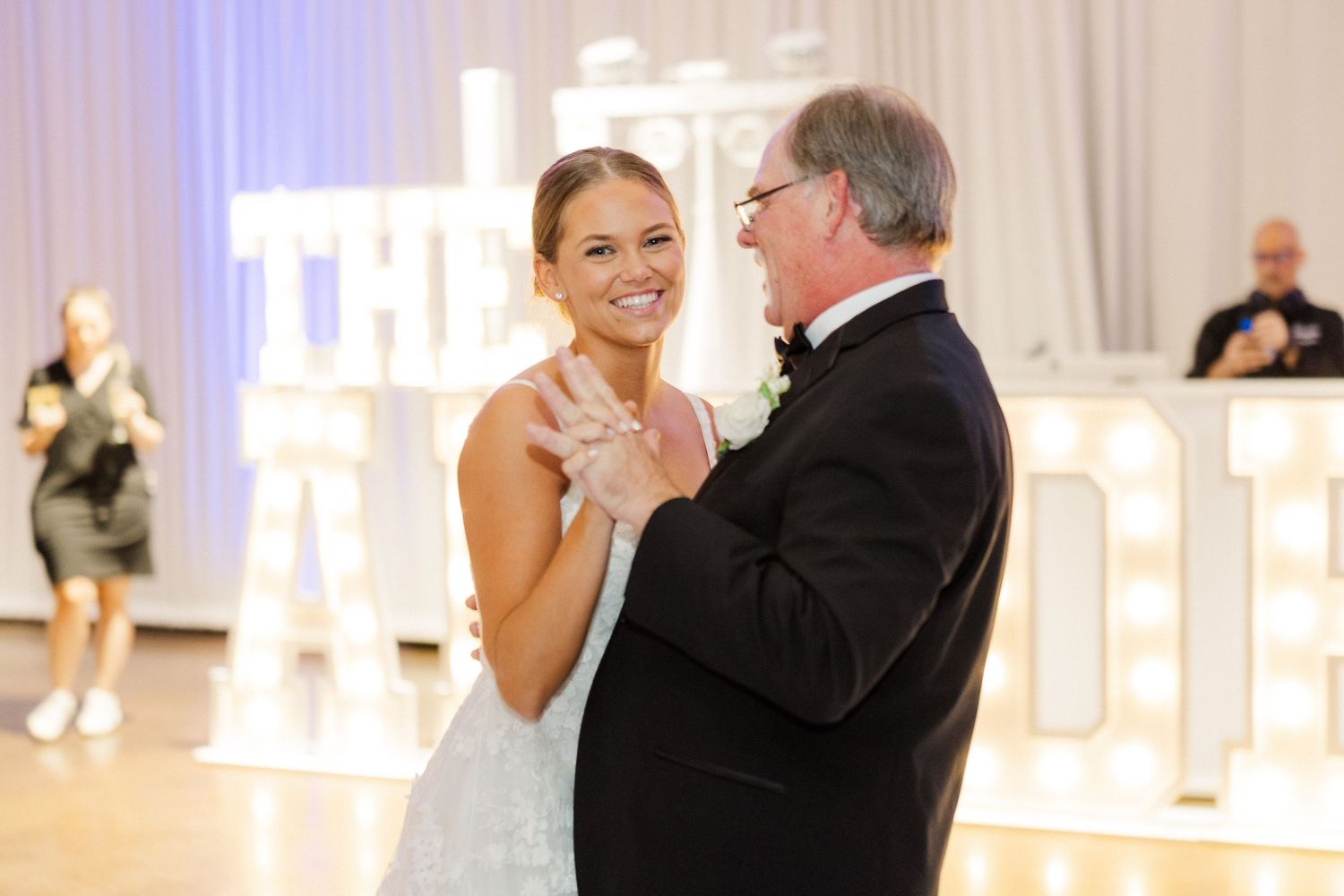 Couple sharing intimate dance moment at wedding reception with backlit white decor.
