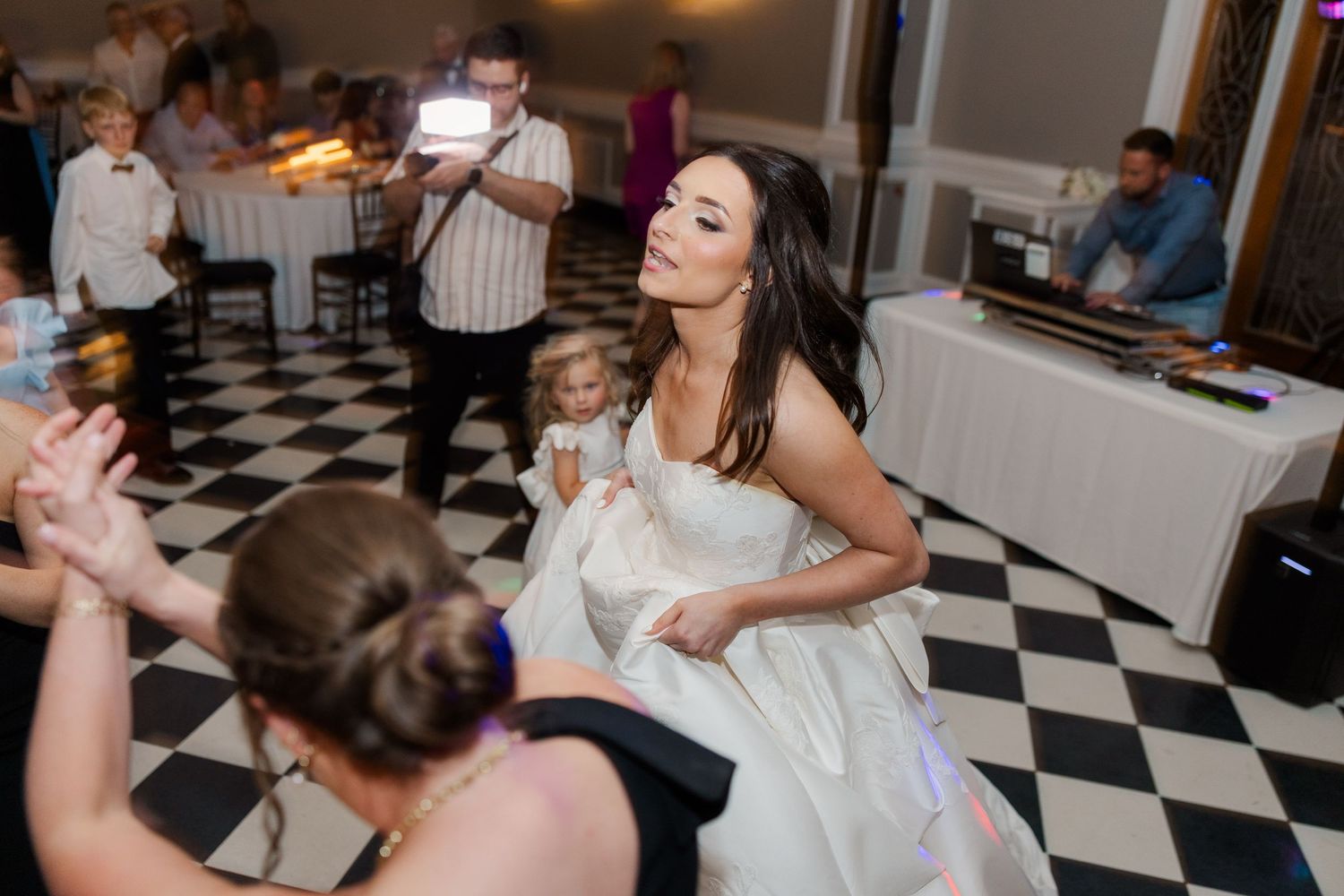 Wedding reception guests dance and celebrate on a black and white checkered dance floor.