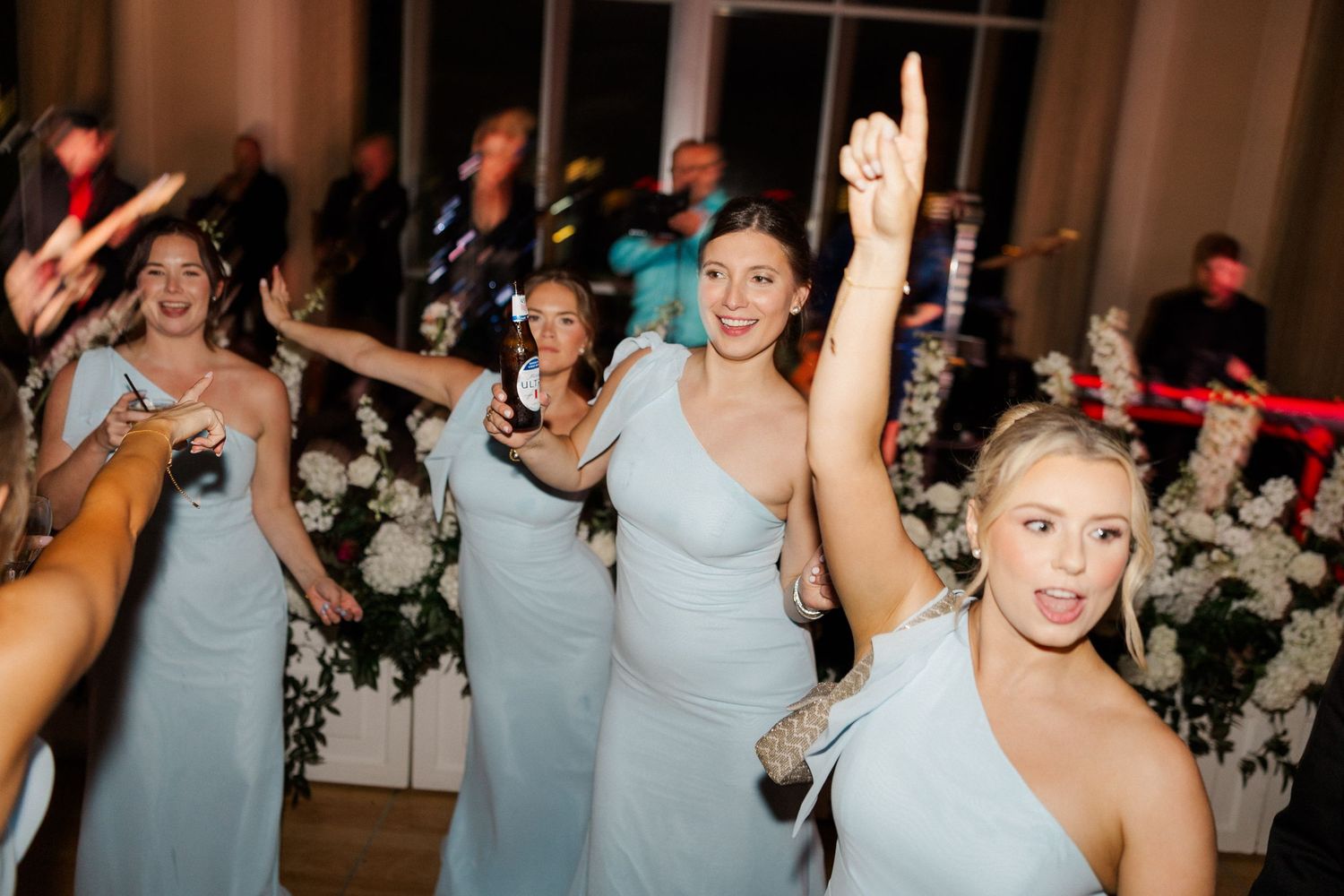 Bridesmaids in light blue dresses dance joyfully at lively wedding reception.