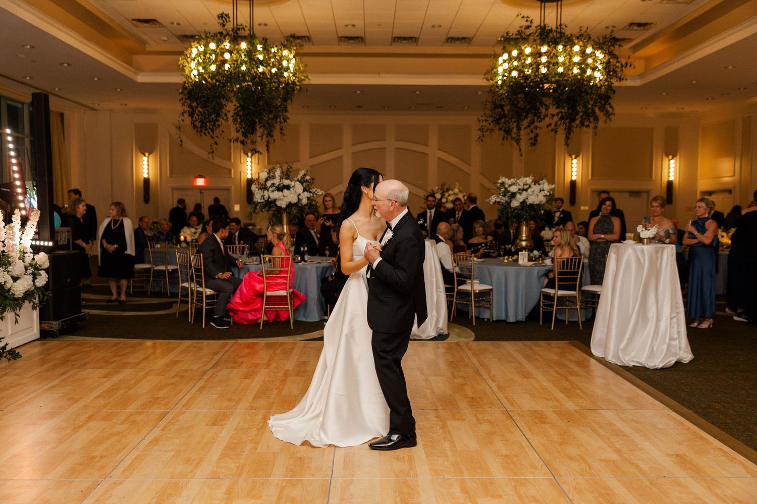 Bride and father share tender first dance in decorated wedding reception ballroom.