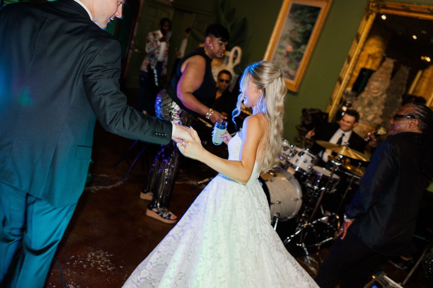 Bride in white lace gown dances energetically with groom near live band at elegant wedding reception.