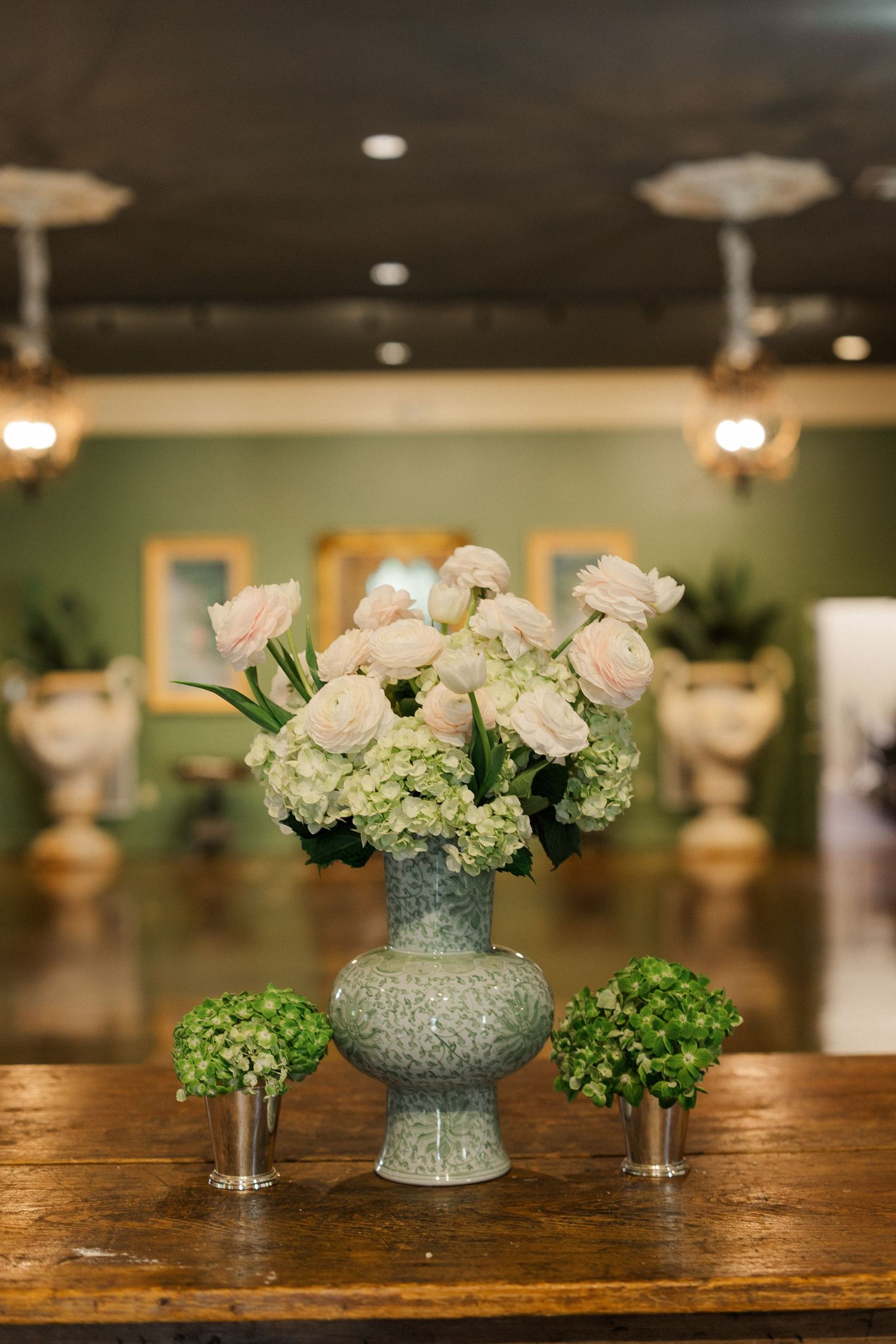 Elegant floral arrangement with white roses and hydrangeas in a stone vase on a wooden table at a wedding venue.