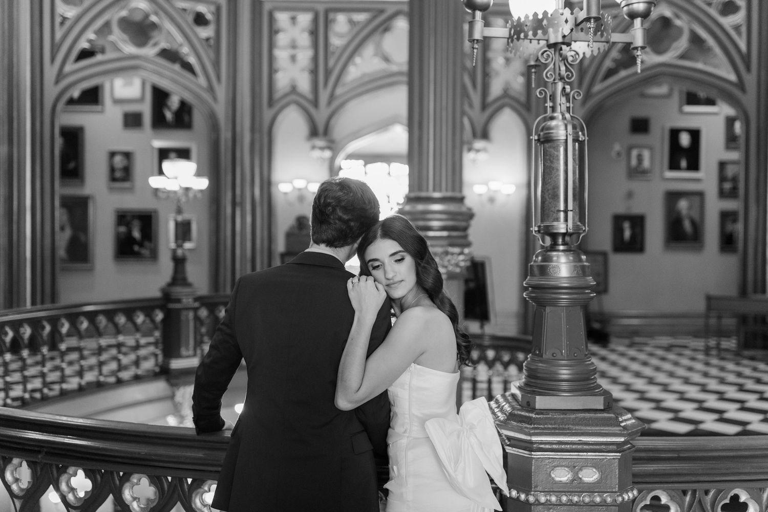A romantic couple shares an intimate moment on an ornate Victorian-style staircase in black and white.